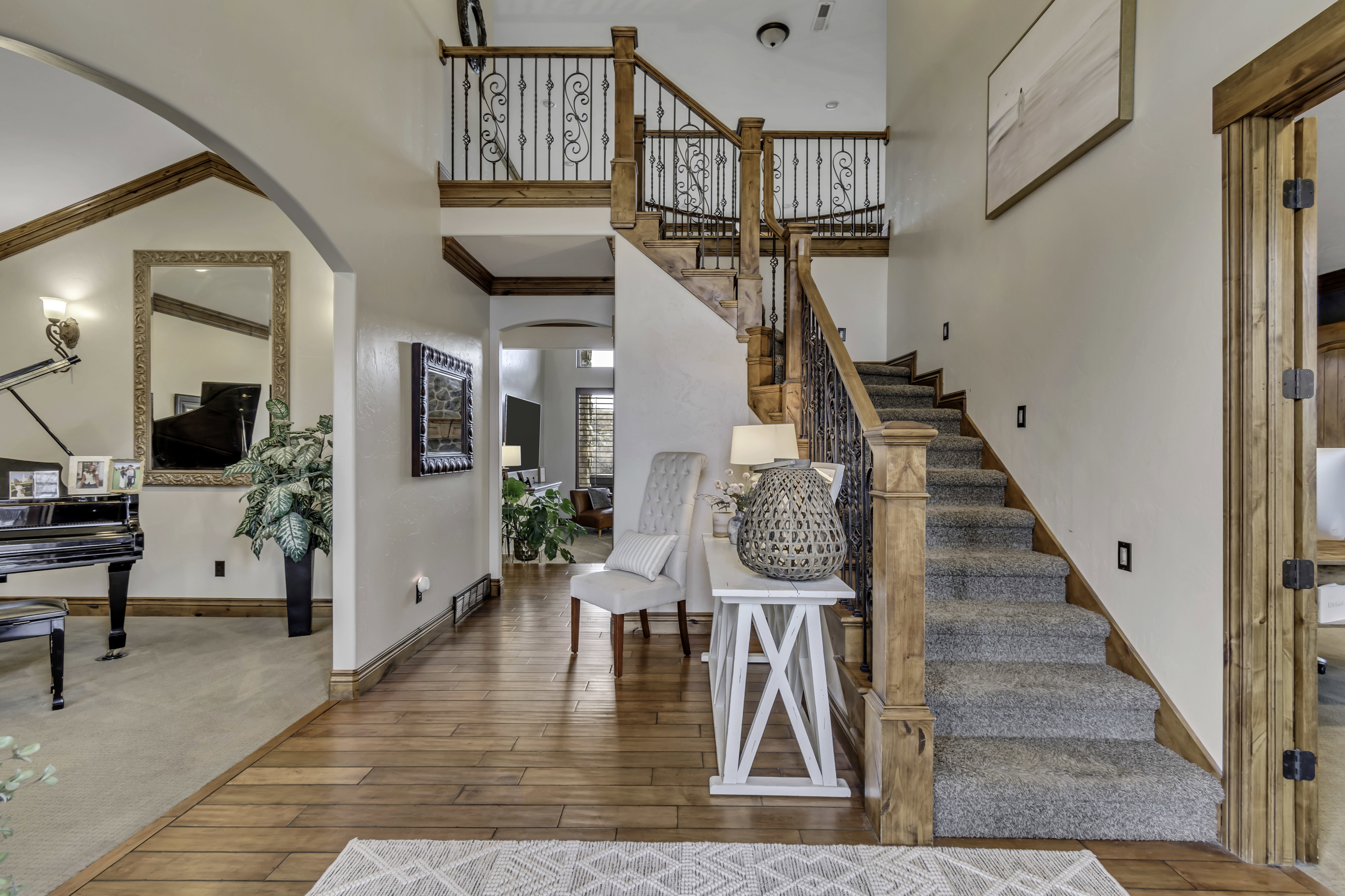 Grand entryway featuring wood-finish flooring, a carpeted staircase with ornate wrought iron and wood balusters, and a second-story landing with matching railing