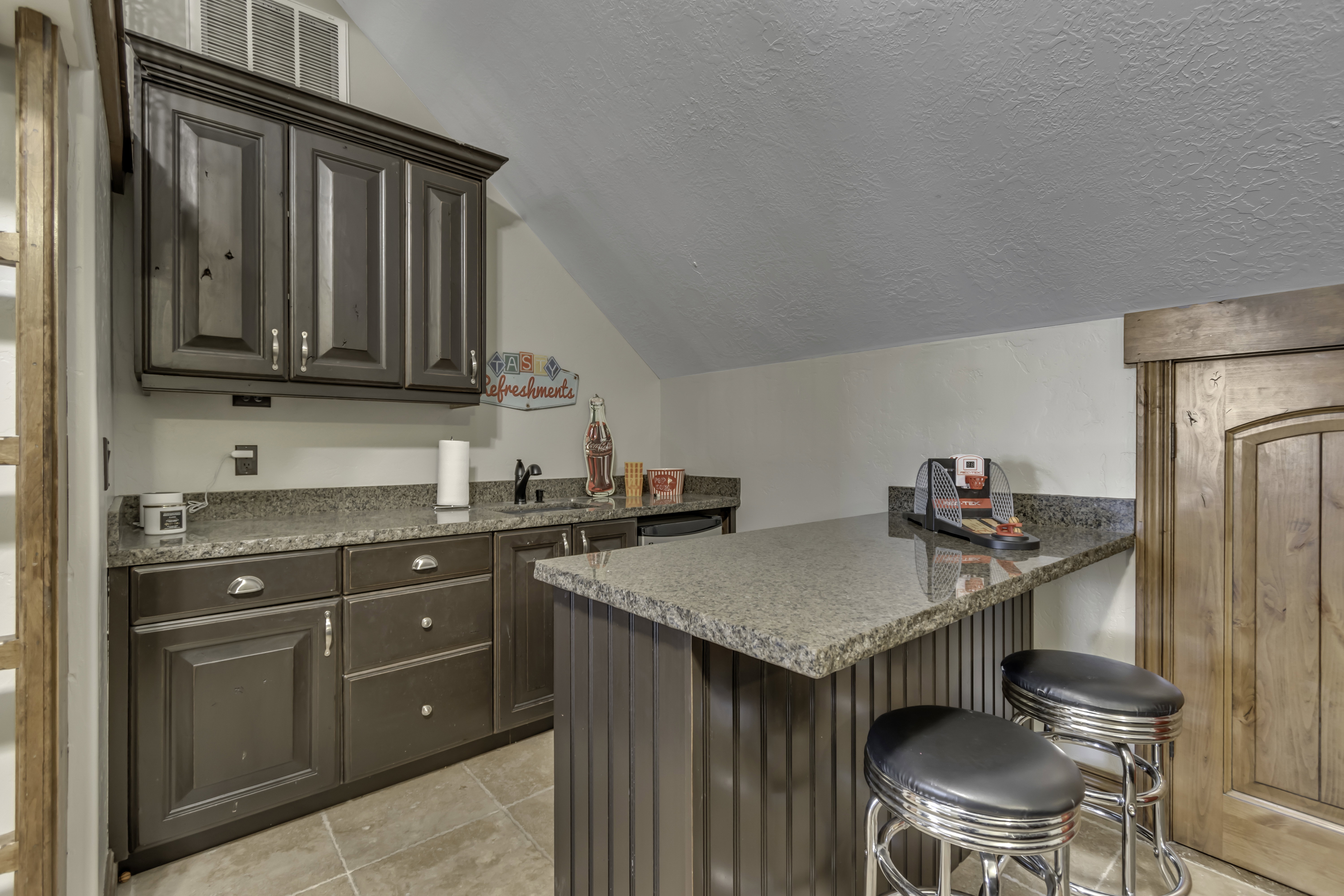 Built-in wet bar featuring dark wood cabinetry, a granite countertop, undermount sink, and tiled flooring