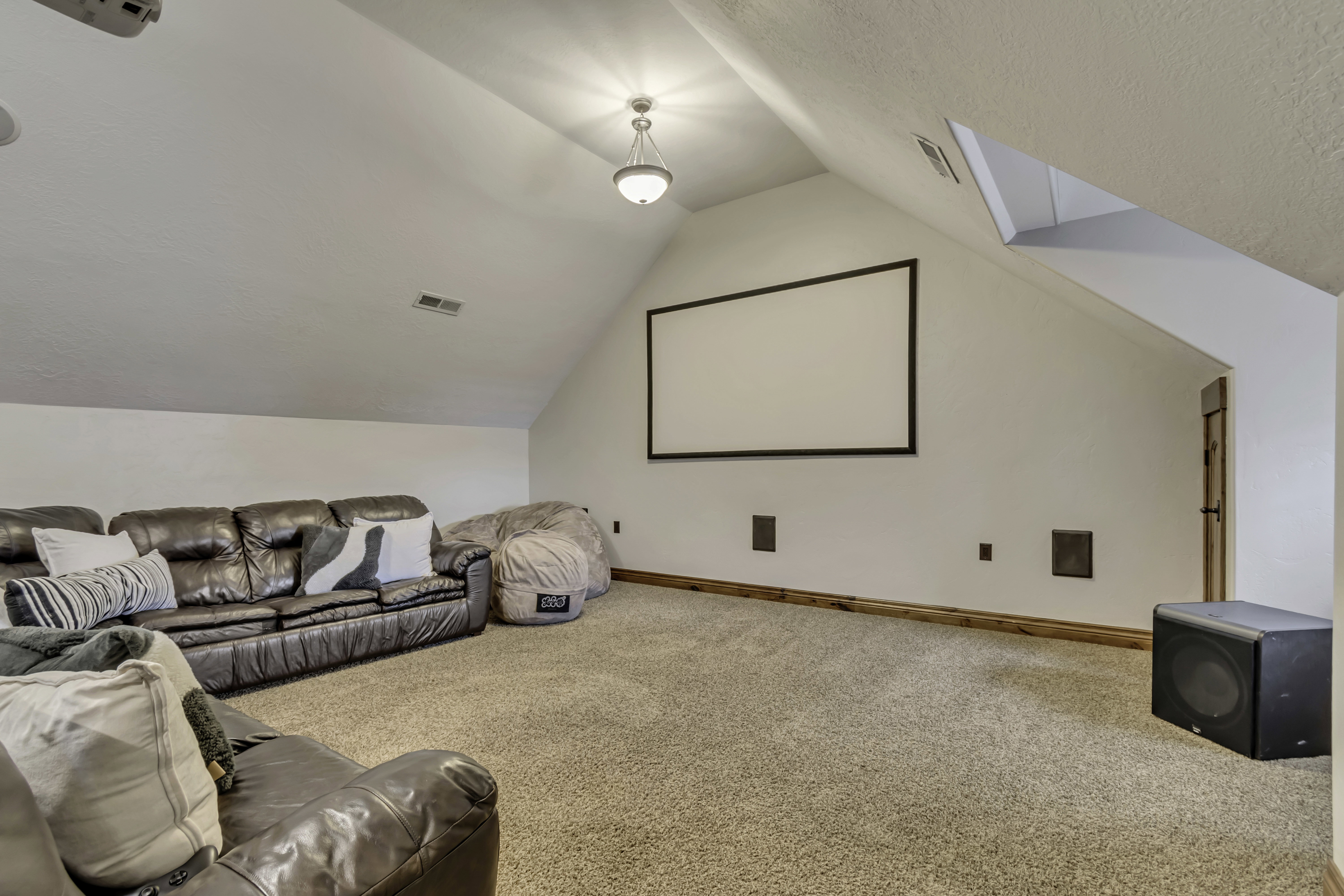 Entertainment room featuring a large projection screen, sloped ceilings, recessed ceiling speakers, and light brown carpeting