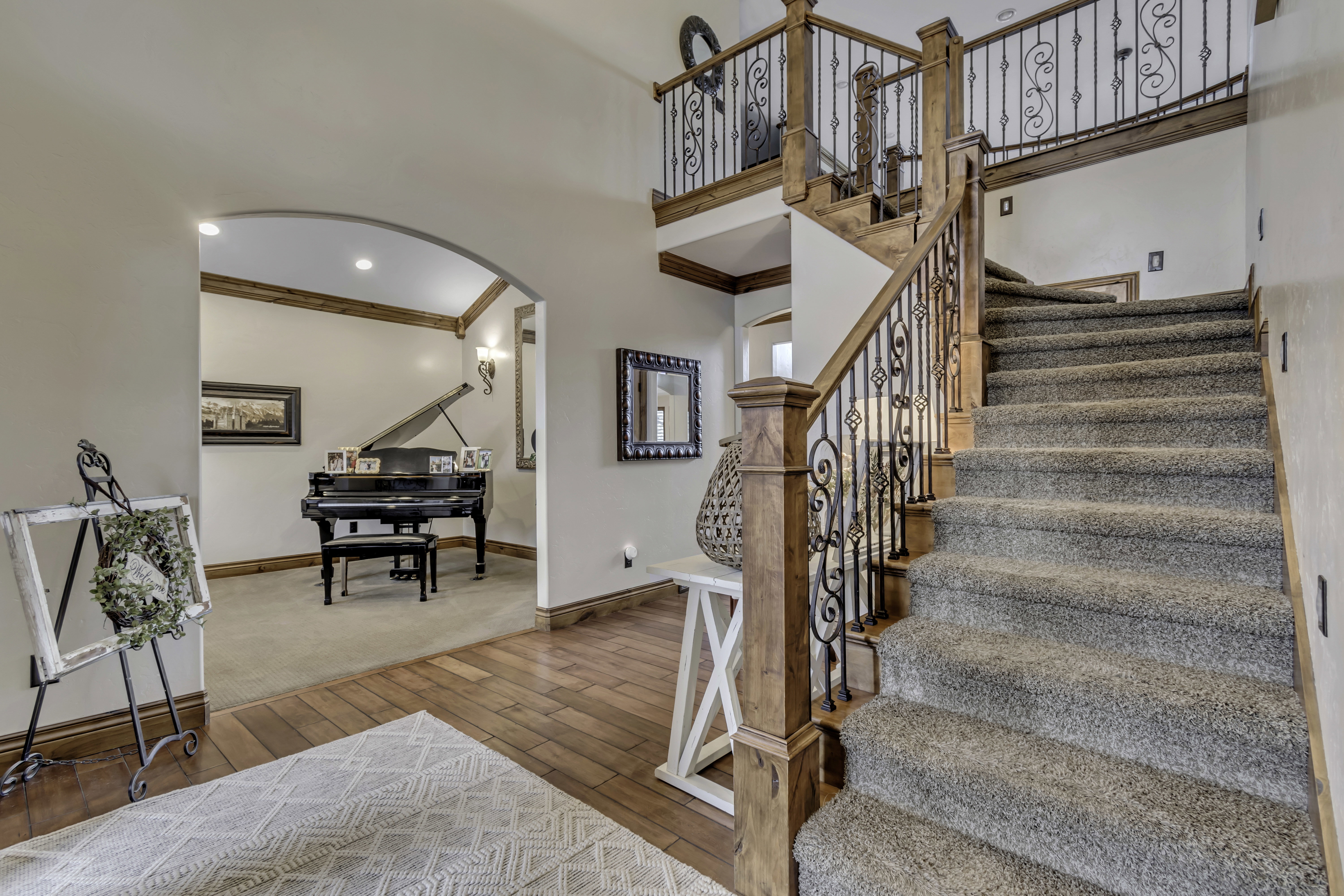 Grand foyer with a carpeted staircase featuring an ornate wrought iron and wood-finish railing