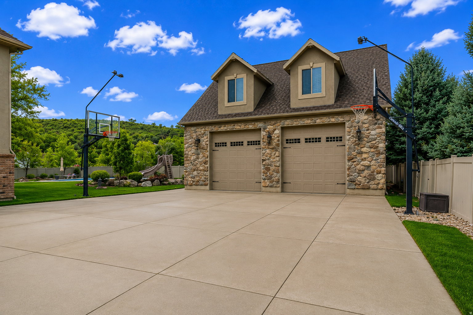 Stone-clad two-car garage with dormer windows and two basketball hoops
