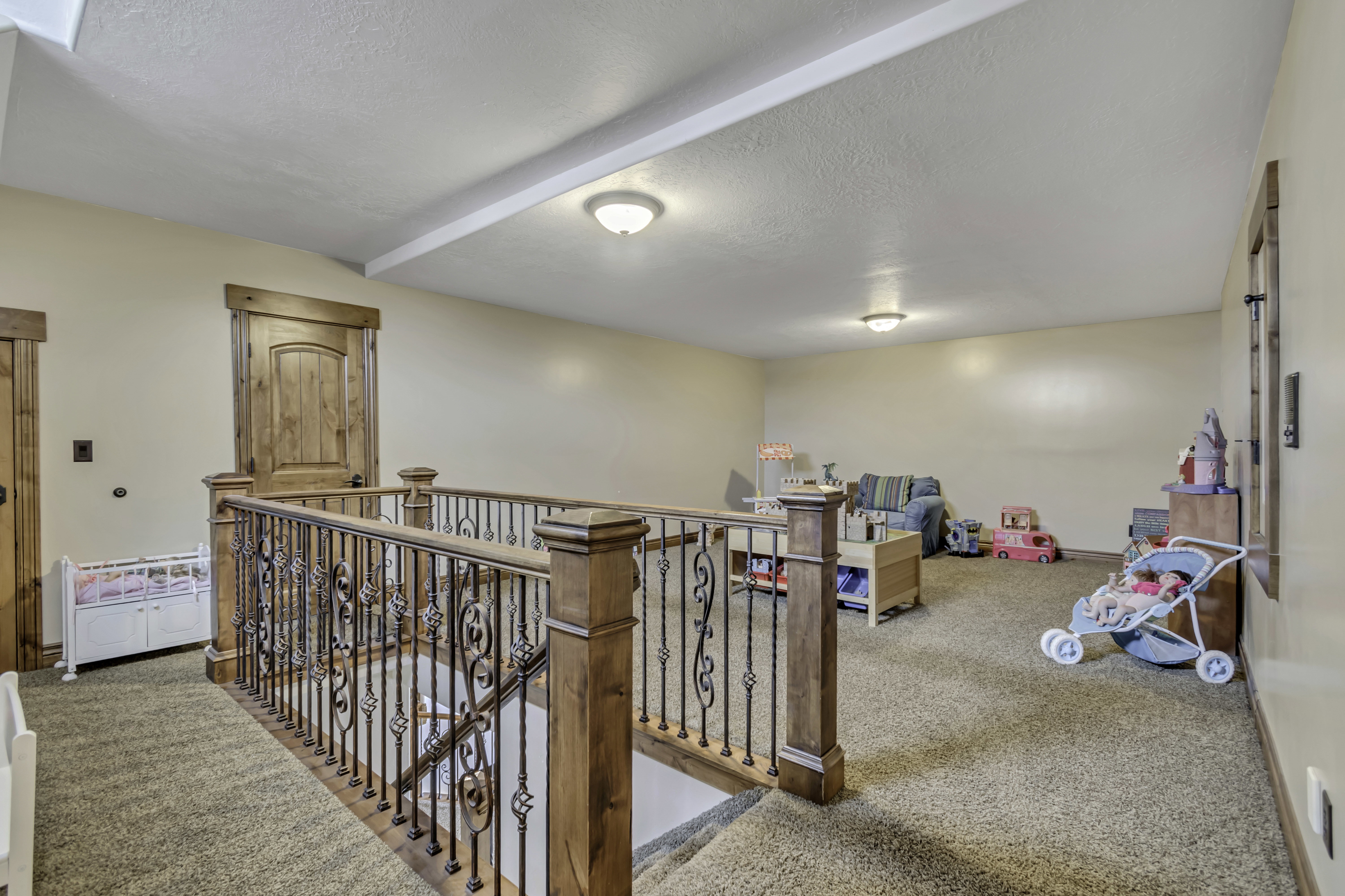 Spacious upper-level landing featuring a custom wrought iron and wood-finish railing, warm beige wall paint, and a textured carpeted floor
