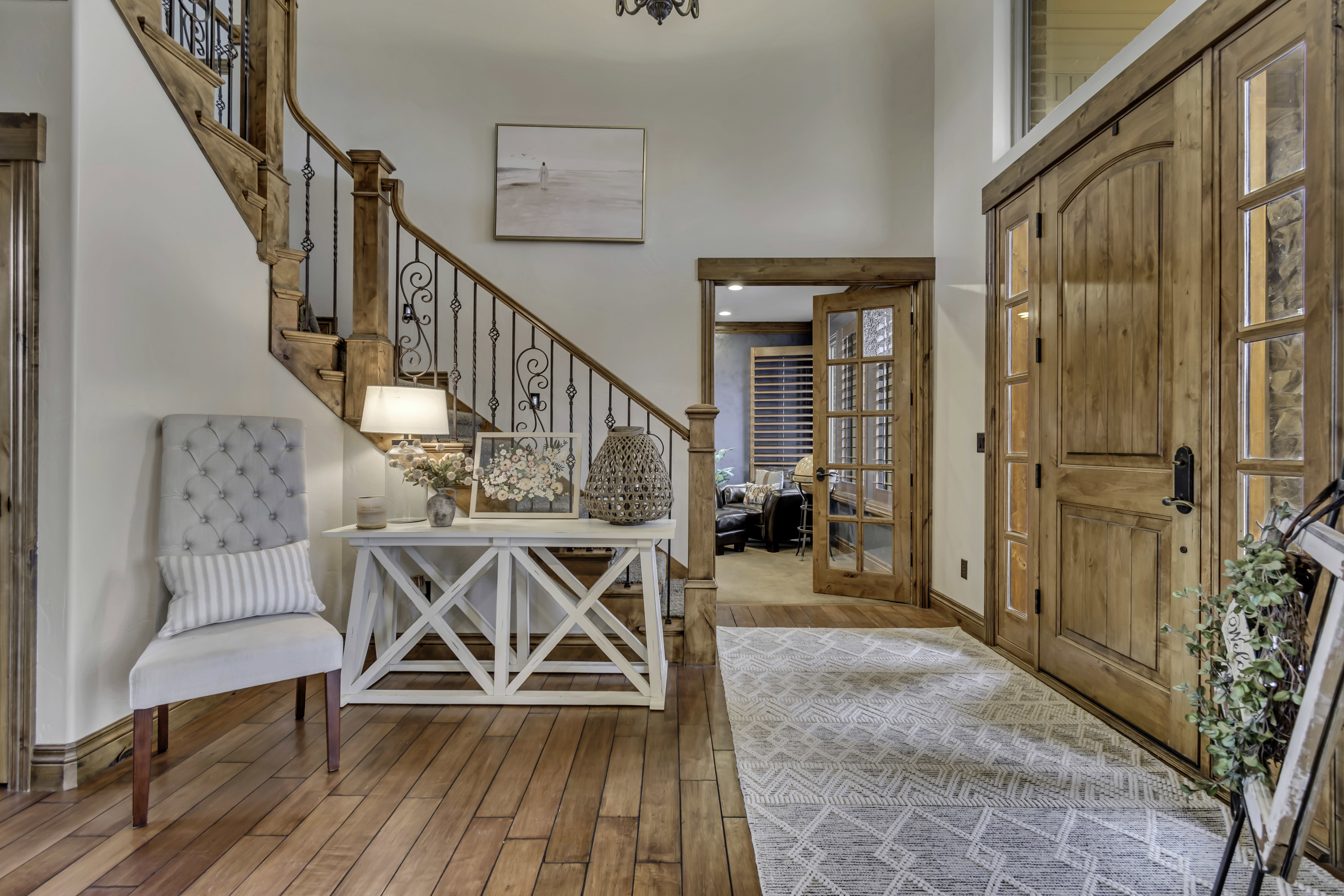 Grand entryway featuring rich wood-finish flooring, a prominent wooden staircase with wrought iron balusters, substantial double entry doors with sidelights, and a wood-framed glass-paned interior door