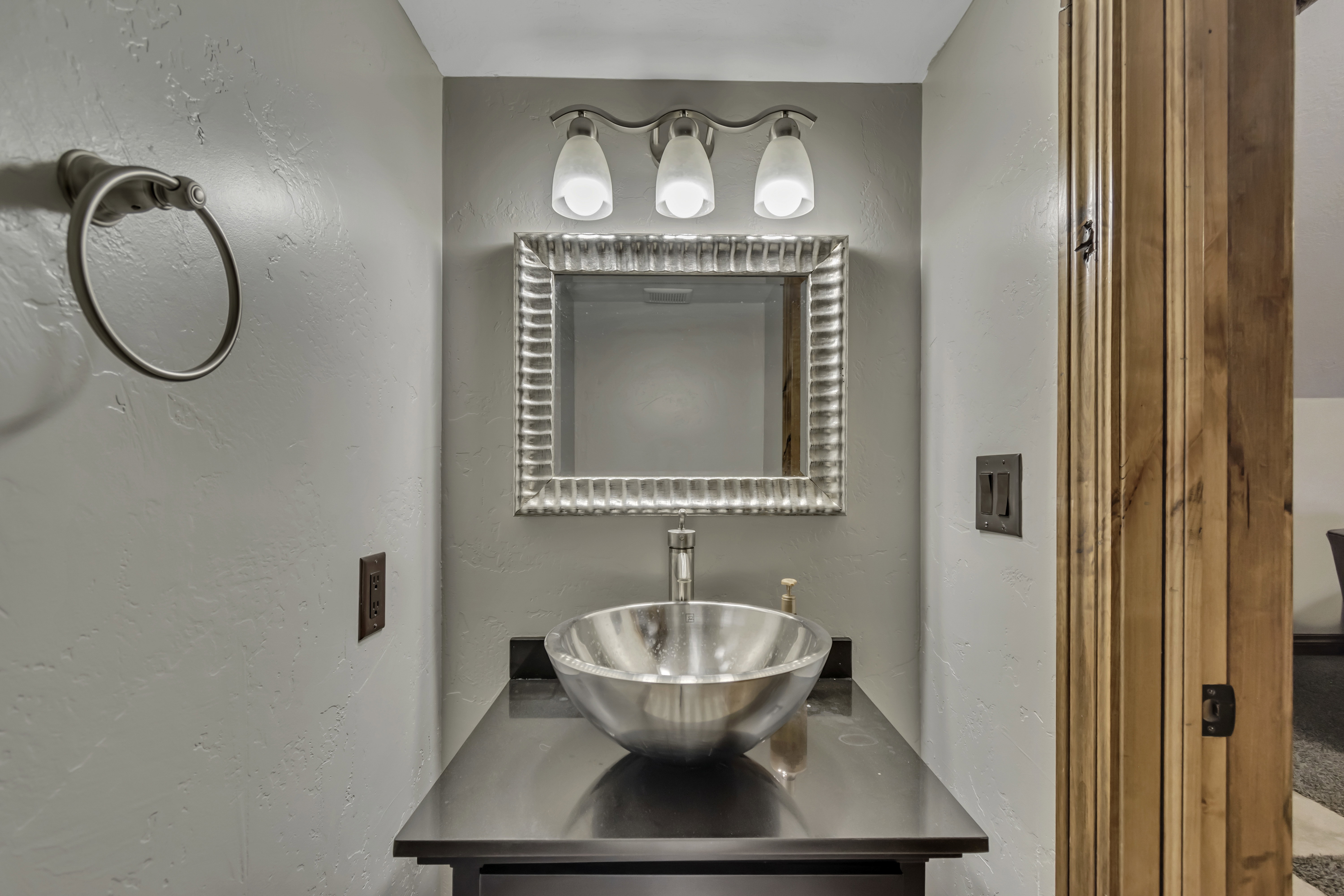 Vanity featuring a vessel sink, dark countertop, and sconce lighting
