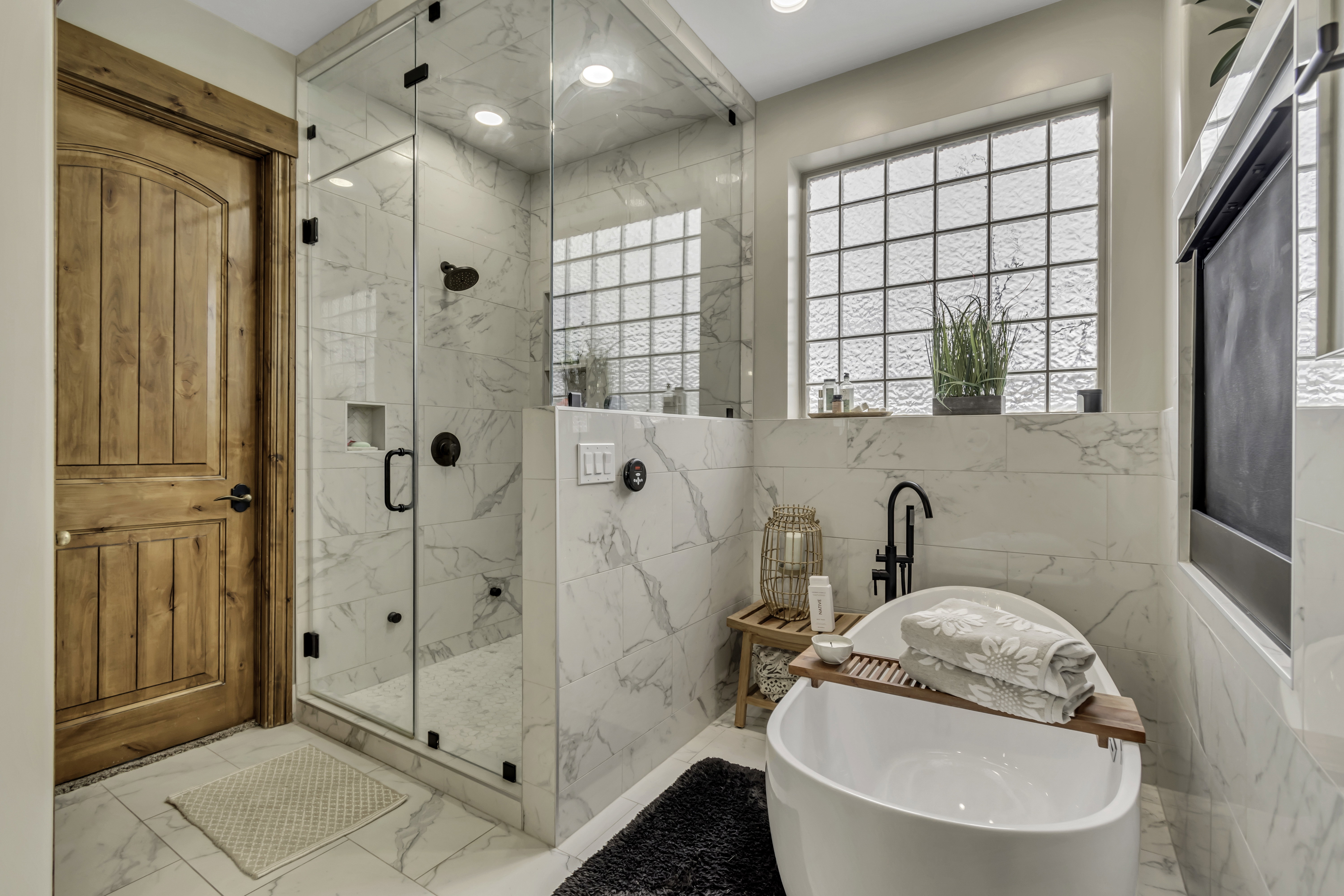 Spacious bathroom featuring a frameless glass shower enclosure, freestanding soaking tub with a floor-mounted faucet, and marble-finish tile flooring and walls