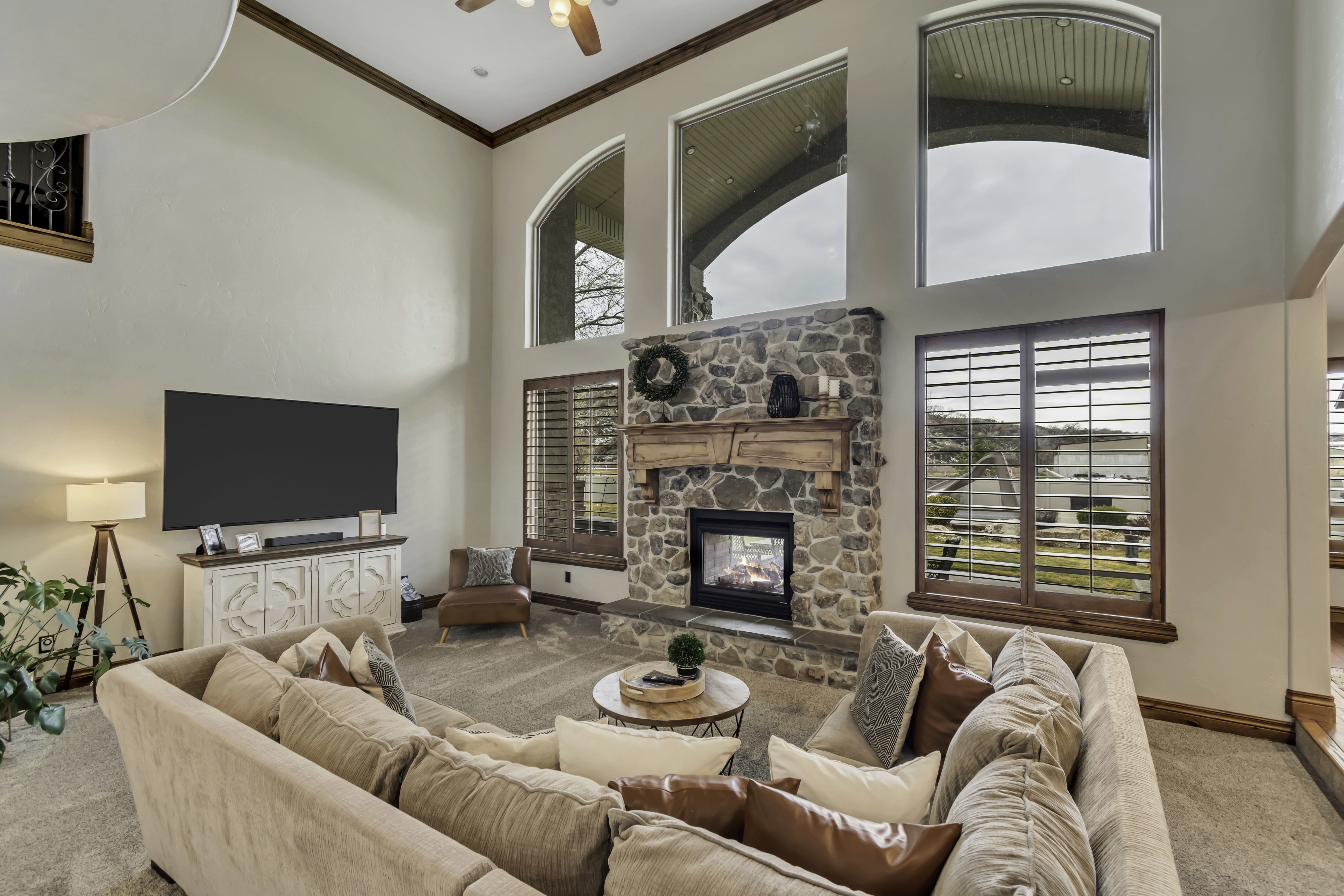 Spacious living area featuring a floor-to-ceiling stone fireplace with a wood-beam mantel, vaulted ceilings, and high arched windows
