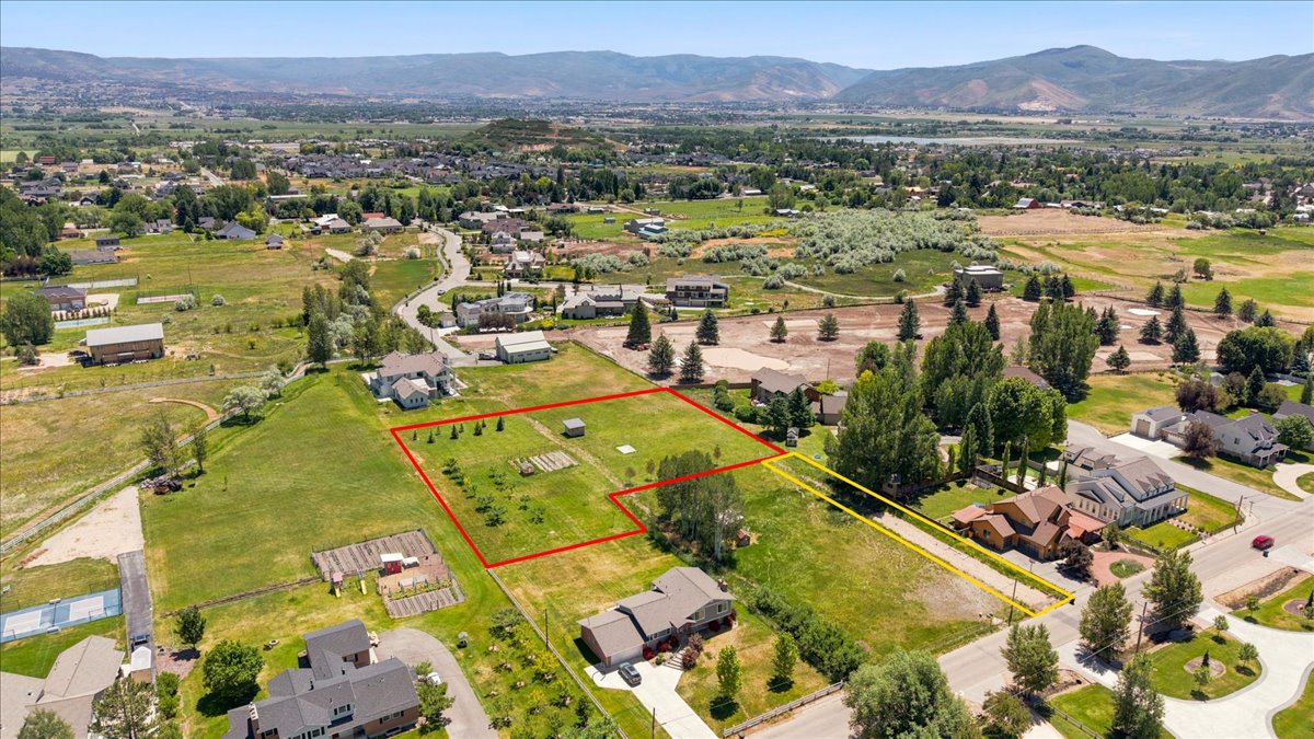 Expansive land parcel with surrounding green space, mature trees, and mountainous terrain in the distance