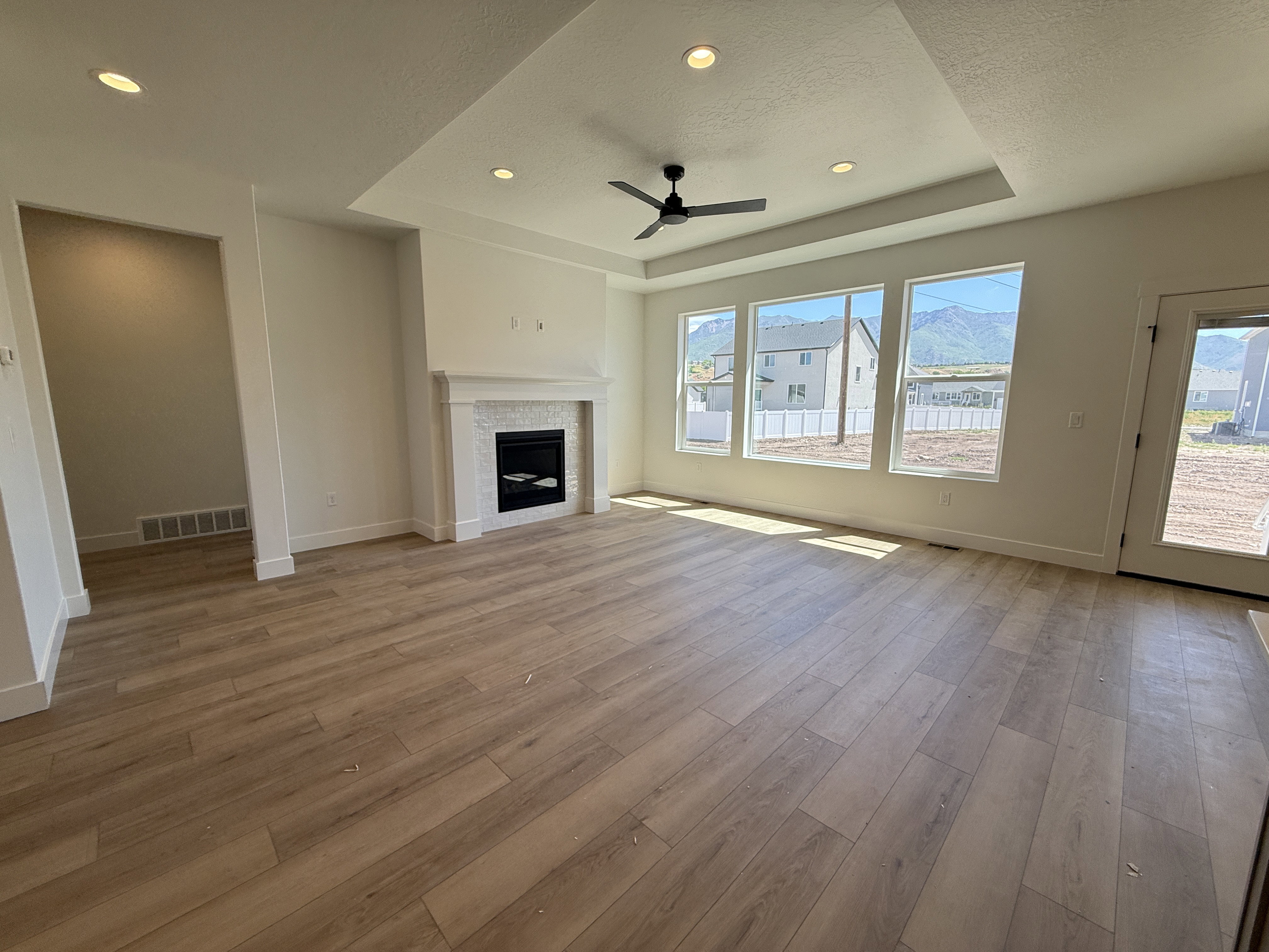 Living area featuring wood-finish flooring, a fireplace with a decorative mantel and tiled surround, a tray ceiling with recessed lighting and a ceiling fan, and large windows with mountain scenery
