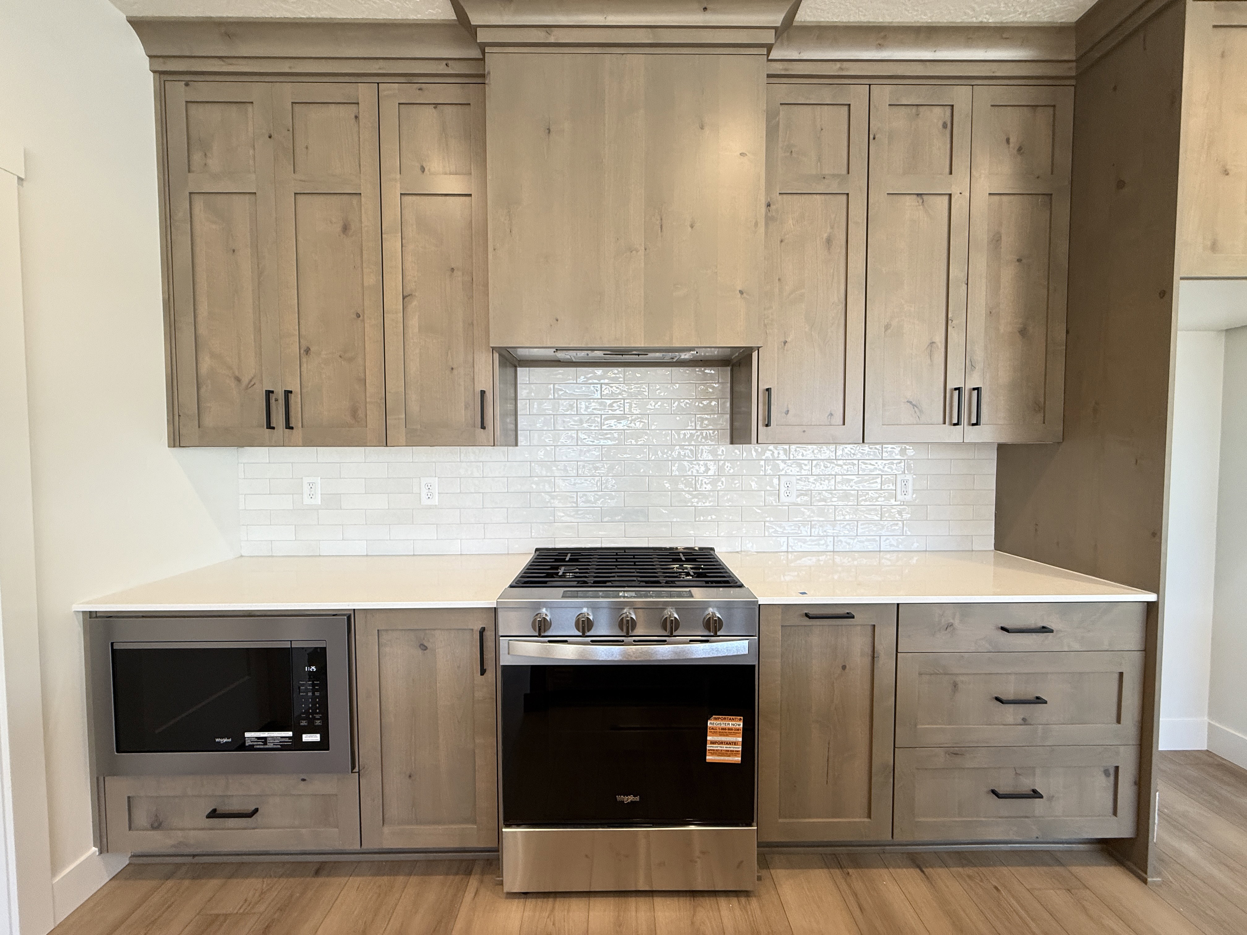 Kitchen featuring light wood-finish cabinetry with black hardware, white subway tile backsplash, and light countertops