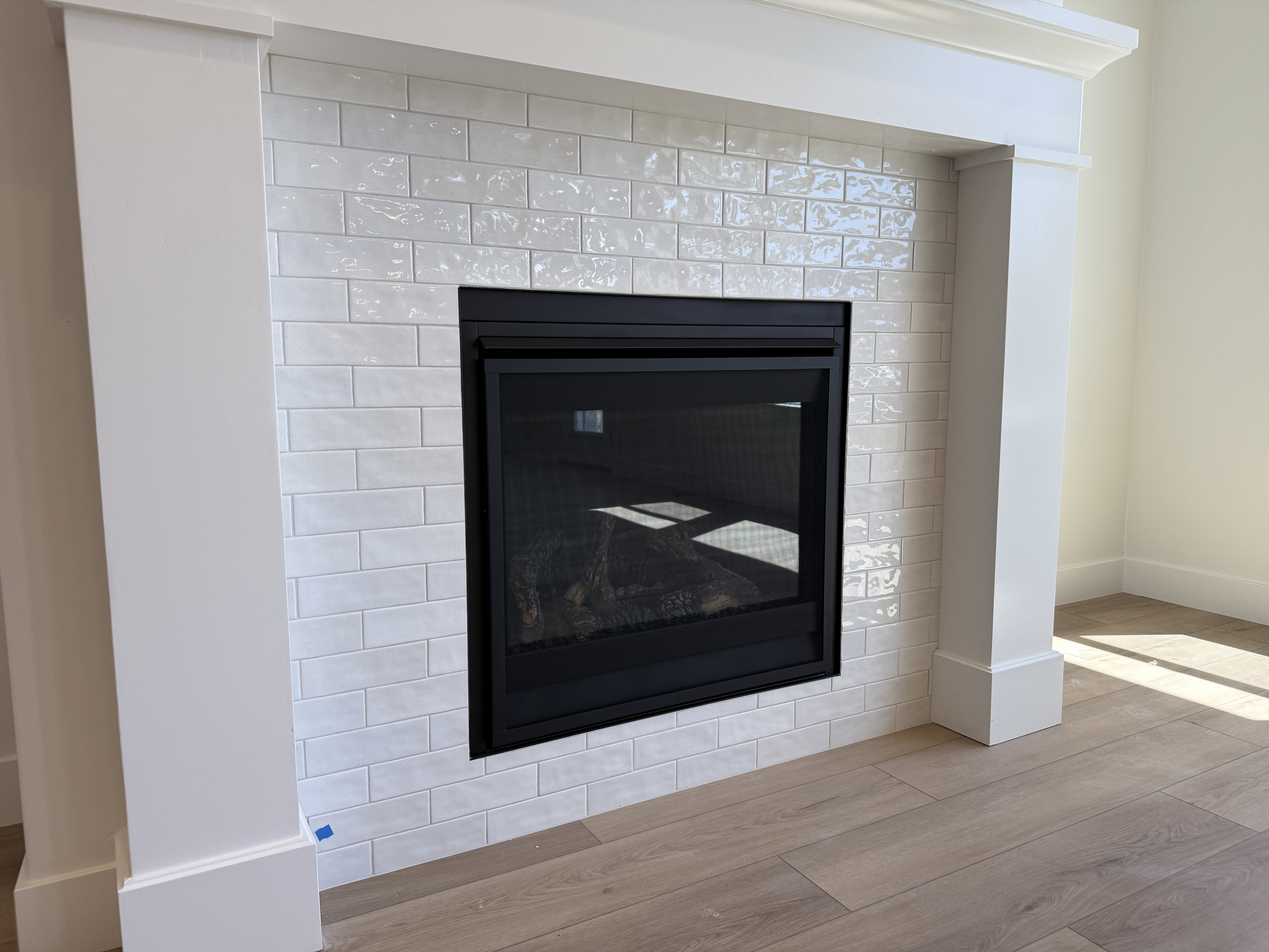 Contemporary fireplace with a black glass-front insert, framed by white subway tile surround and a substantial white mantel