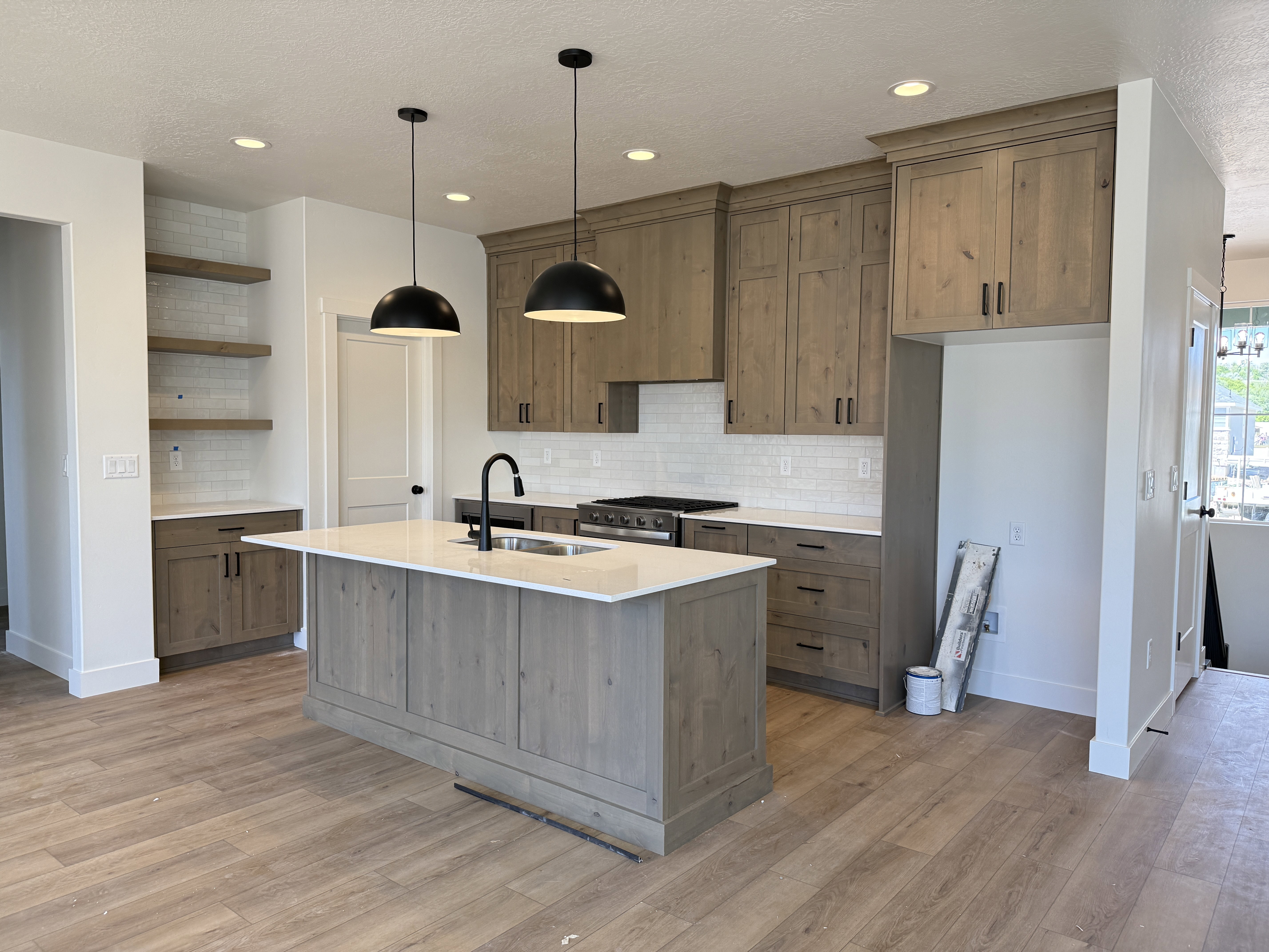 Spacious kitchen featuring an expansive center island with an undermount sink, light wood-finish cabinetry, white subway tile backsplash, and wood-finish flooring