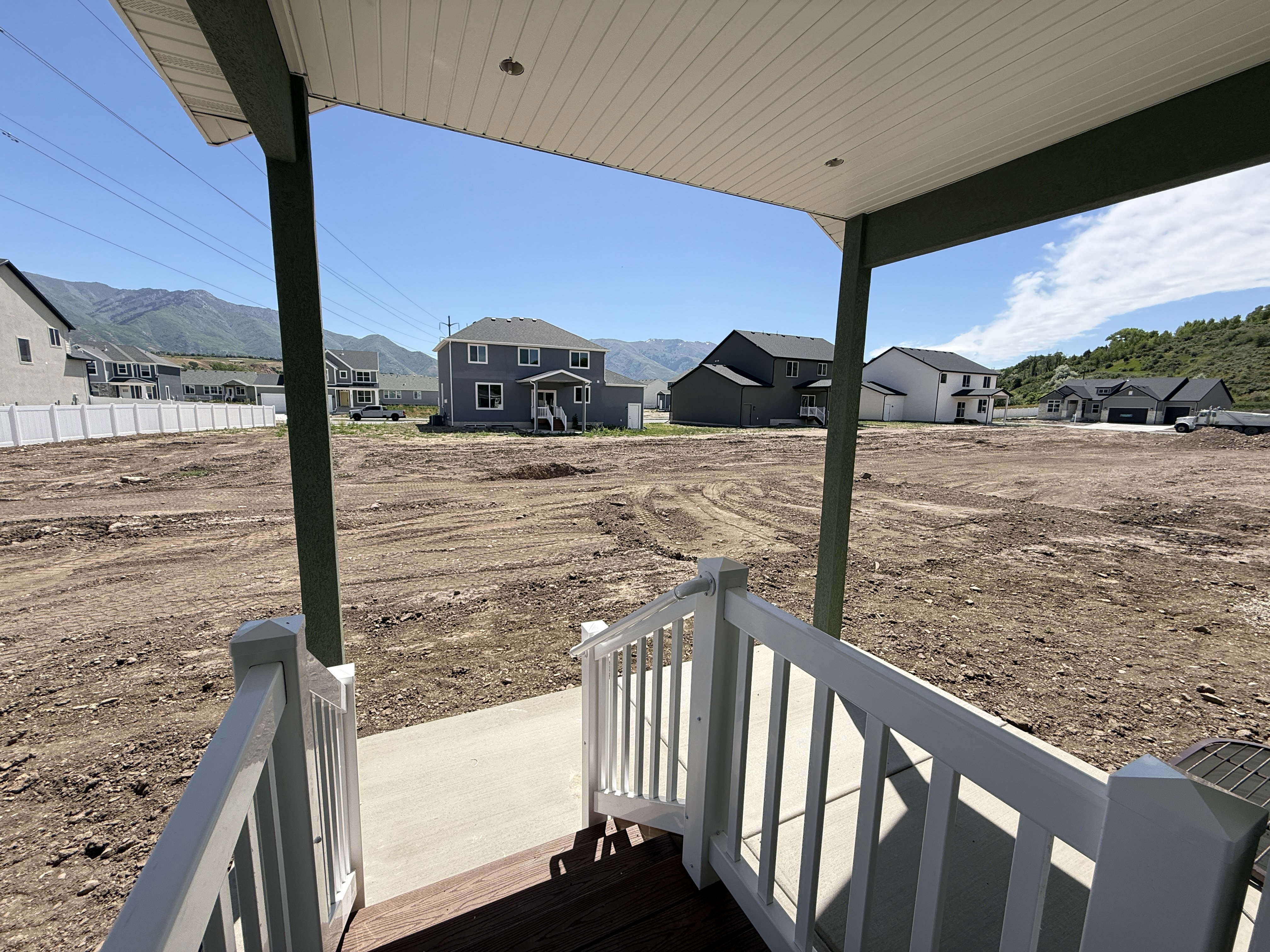 Front porch with white railings and a dark wood-finish deck, overlooking undeveloped land