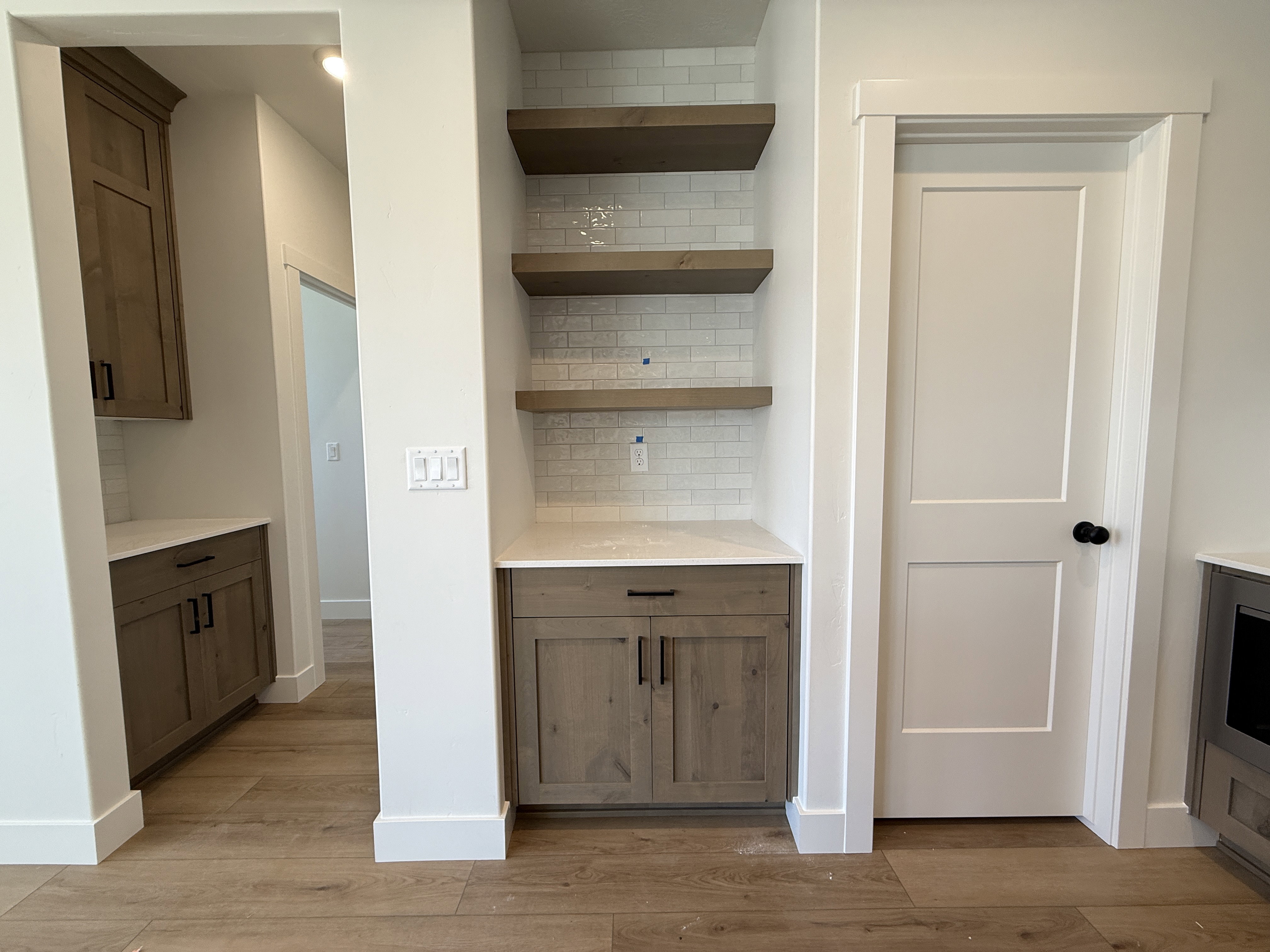 Built-in shelving unit with three floating wood-finish shelves, subway tile backsplash, and a light-toned countertop