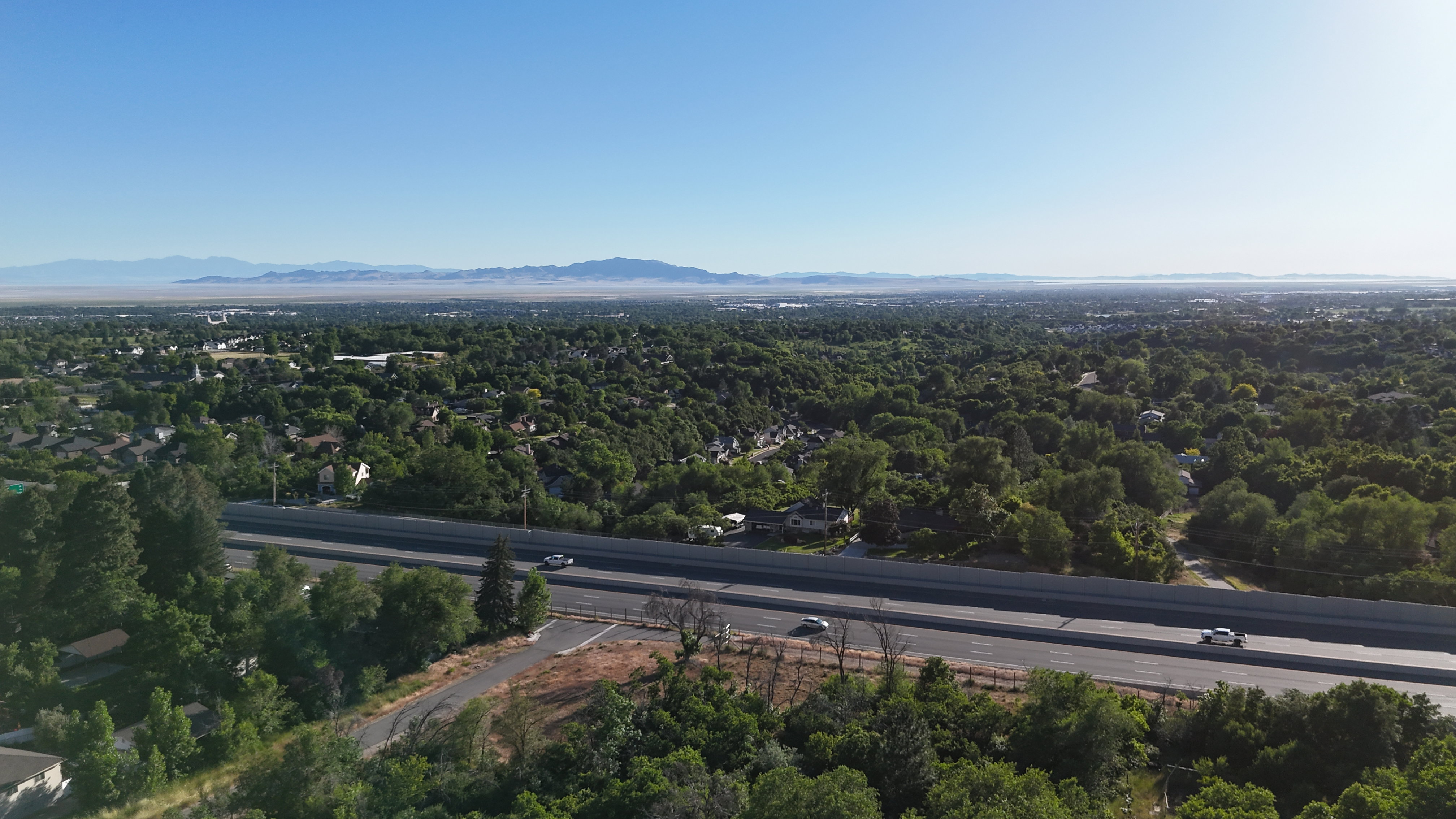 Expansive aerial perspective showcasing a wide two-lane roadway bordered by lush green foliage