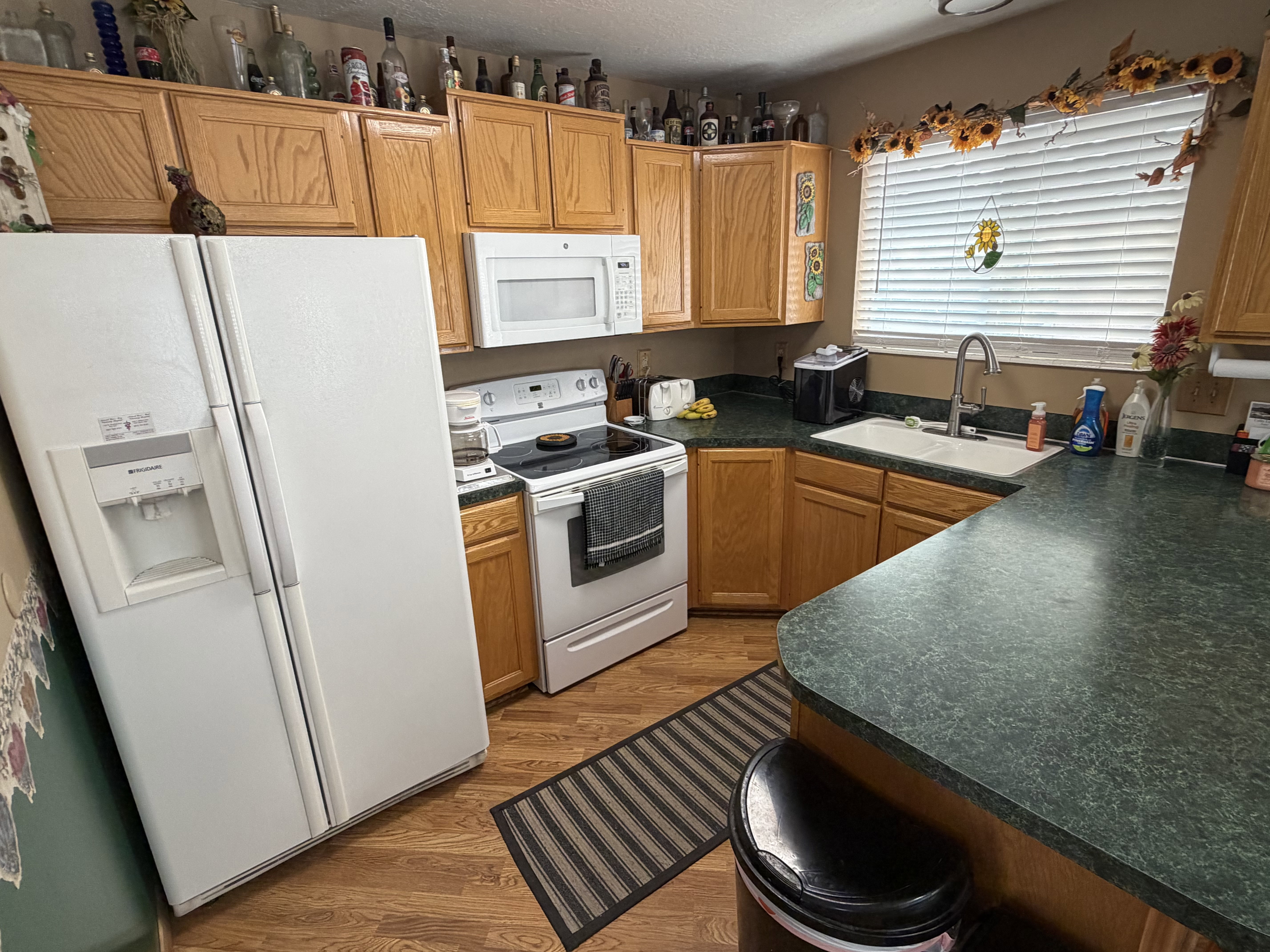 Kitchen featuring wood-finish flooring, oak cabinetry, white appliances, and a double-basin sink
