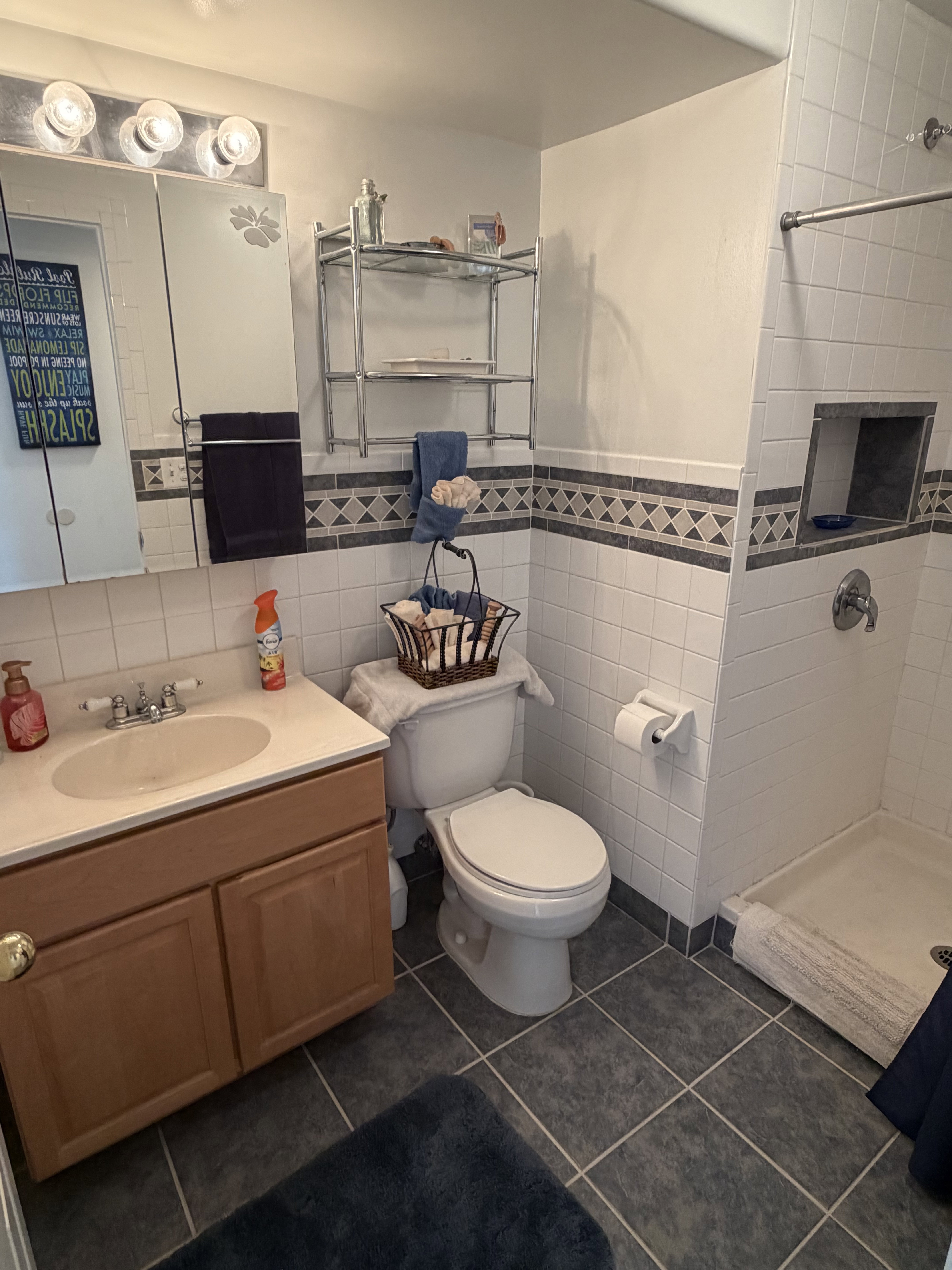 Bathroom featuring a wood-finish vanity with an integrated sink, a medicine cabinet with vanity lighting, and a tiled shower with a built-in niche