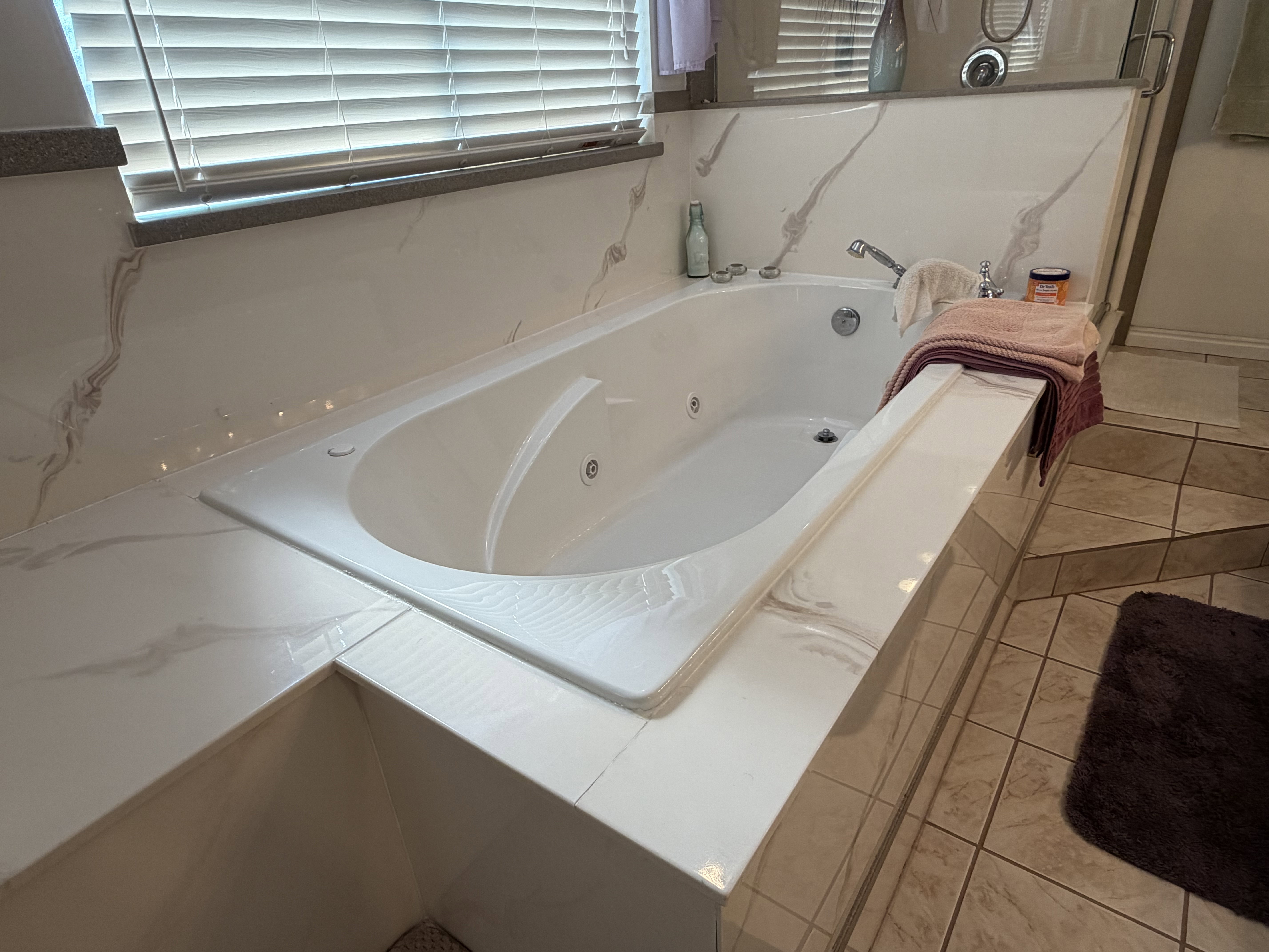 Integrated soaking tub featuring a tiled surround with a marble-effect finish, chrome fixtures, and a tiled floor