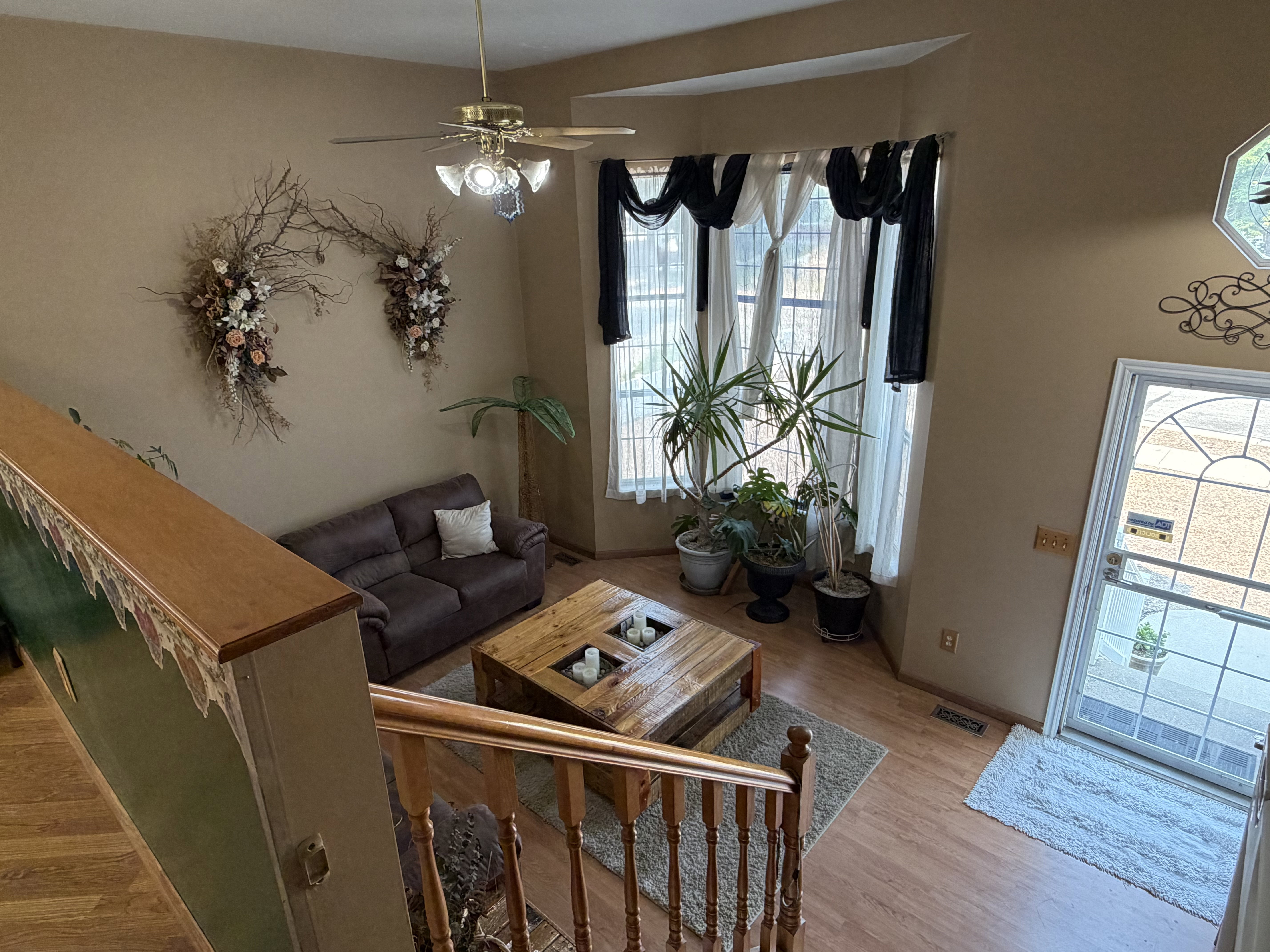 Vaulted ceiling living area featuring wood-finish flooring, bay windows, and a ceiling fan