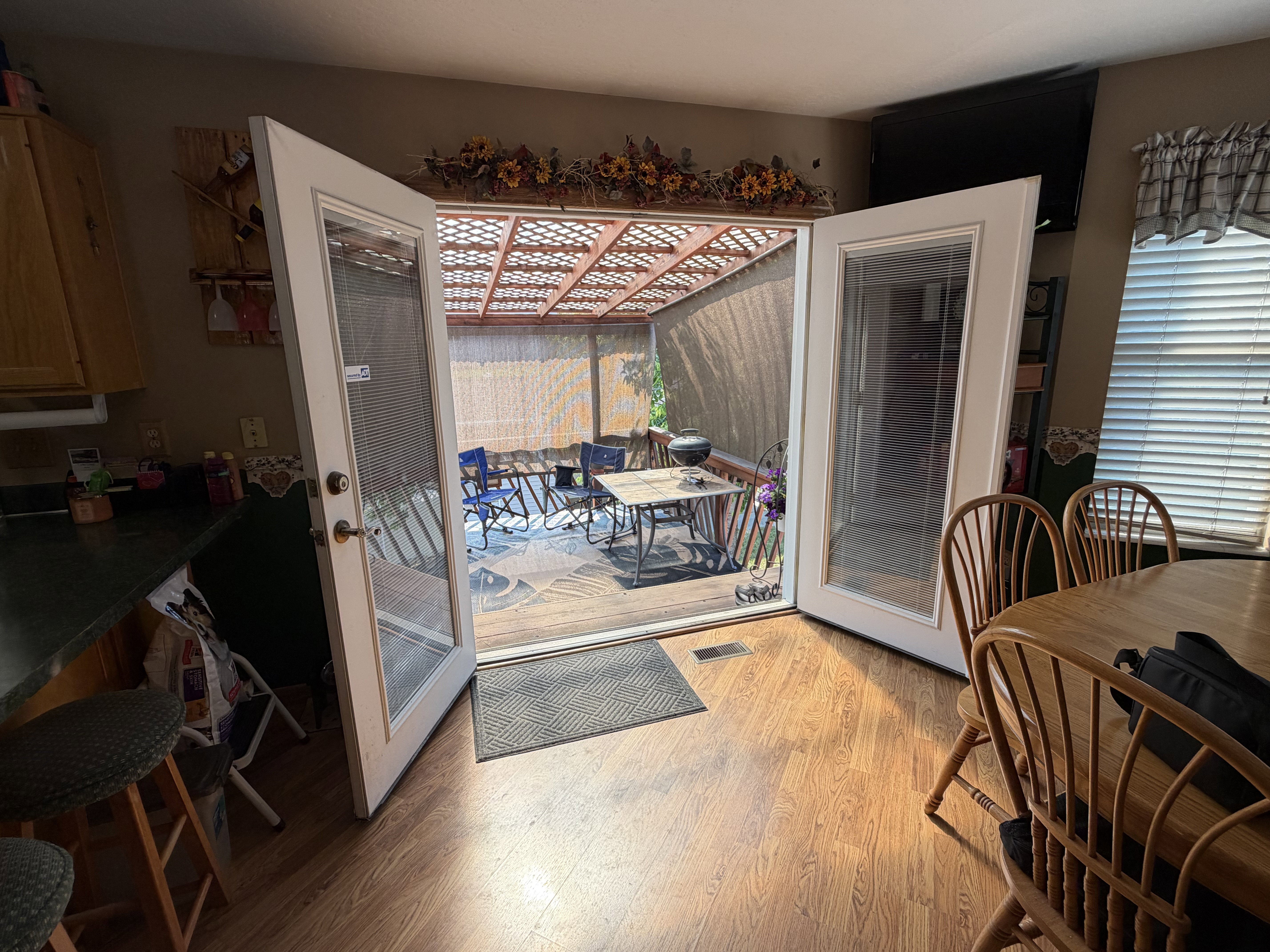 Wood-finish flooring throughout, with double glass-panel doors opening to an outdoor patio featuring a slatted pergola cover