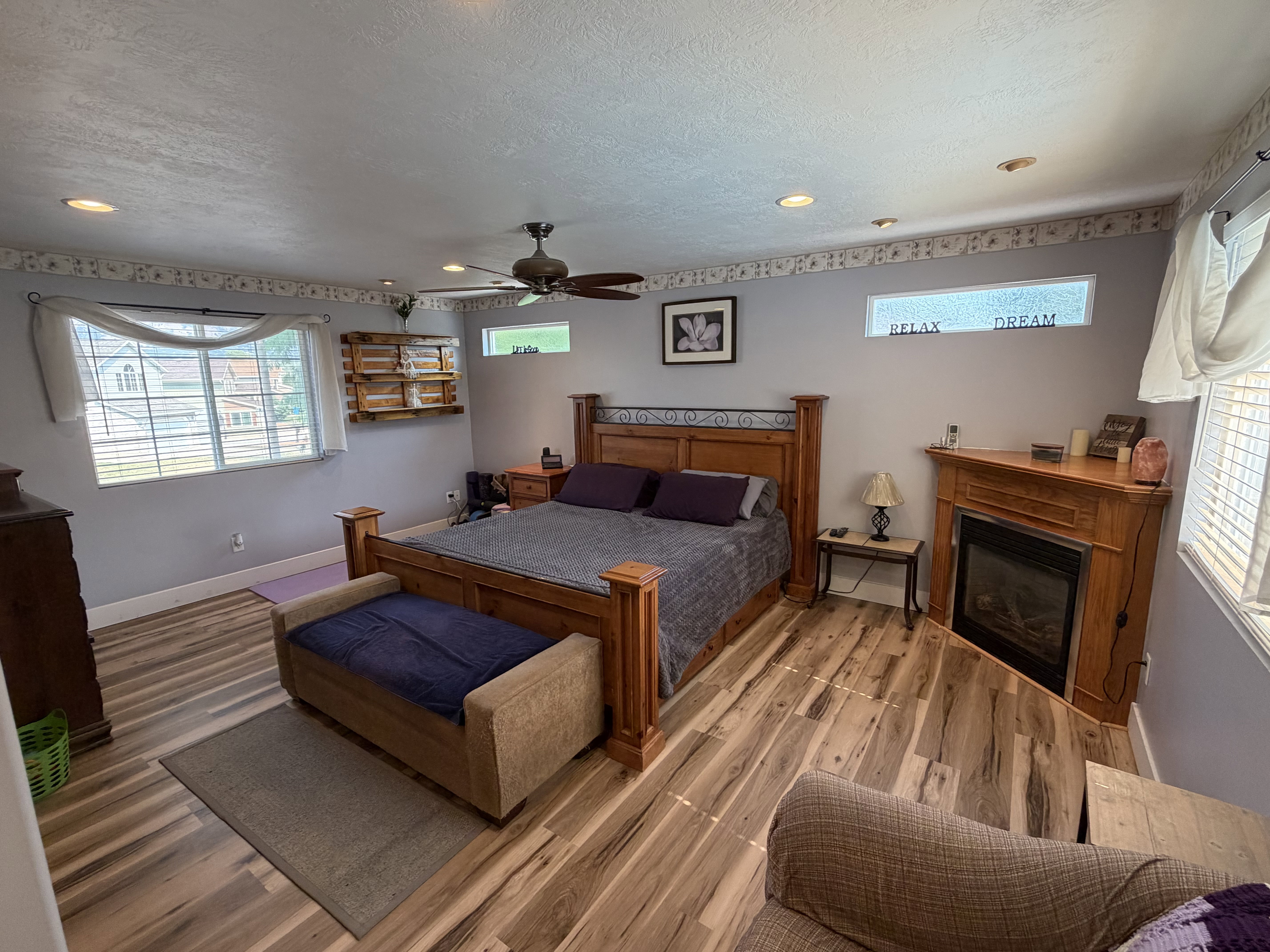 Spacious room featuring wood-finish flooring, a corner fireplace with wood surround, multiple windows for natural light, recessed lighting, and a ceiling fan