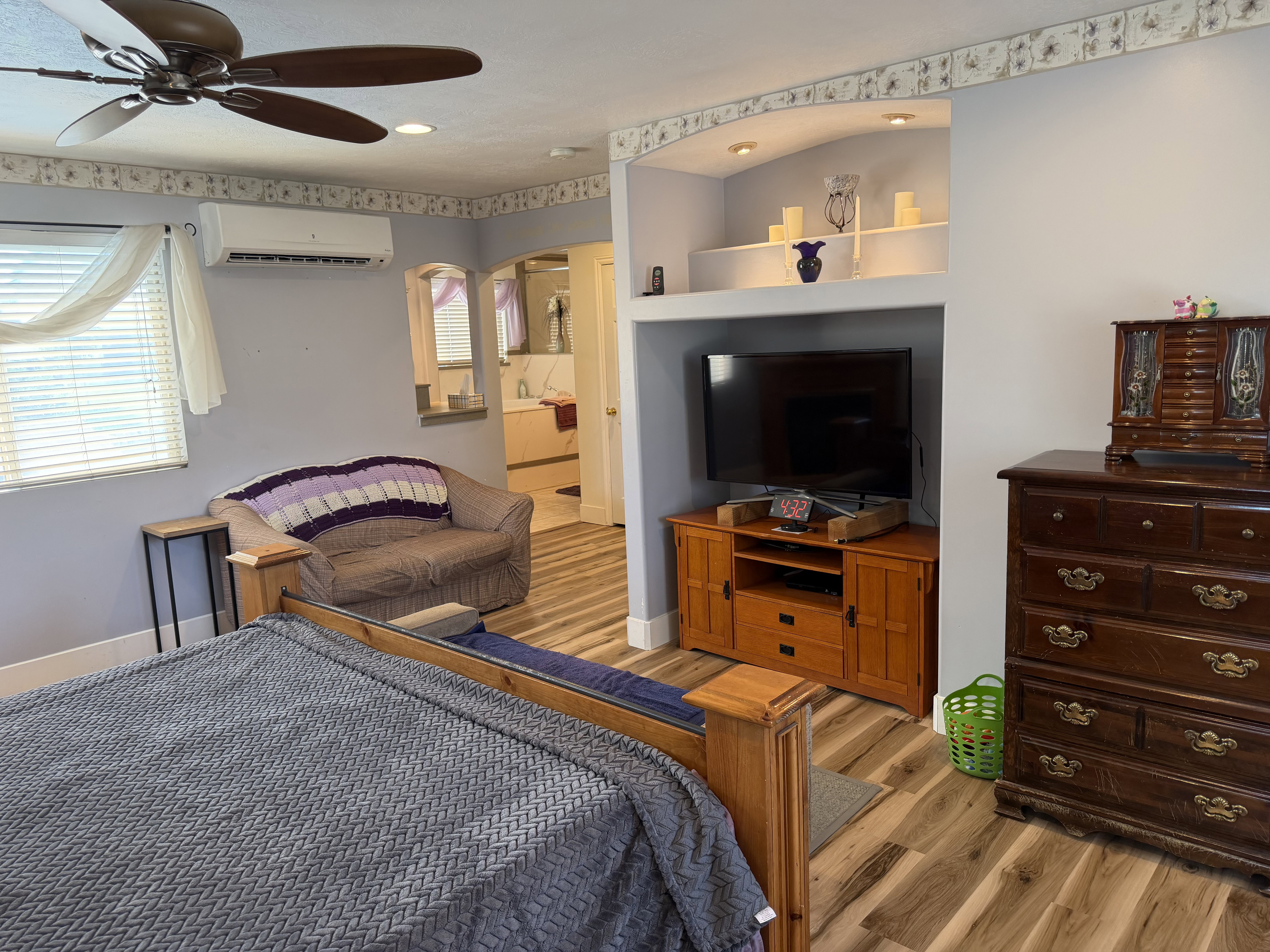 Bedroom featuring wood-finish flooring, a ceiling fan, a mini-split air conditioning unit, and a built-in entertainment niche with accent lighting