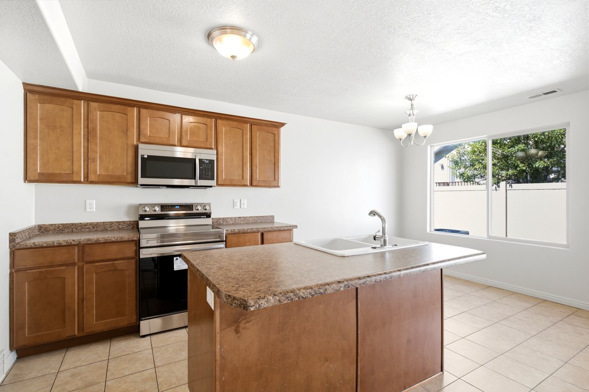 Kitchen featuring a central island with an integrated double sink, wood-finish cabinetry, stainless steel appliances, and a tiled floor