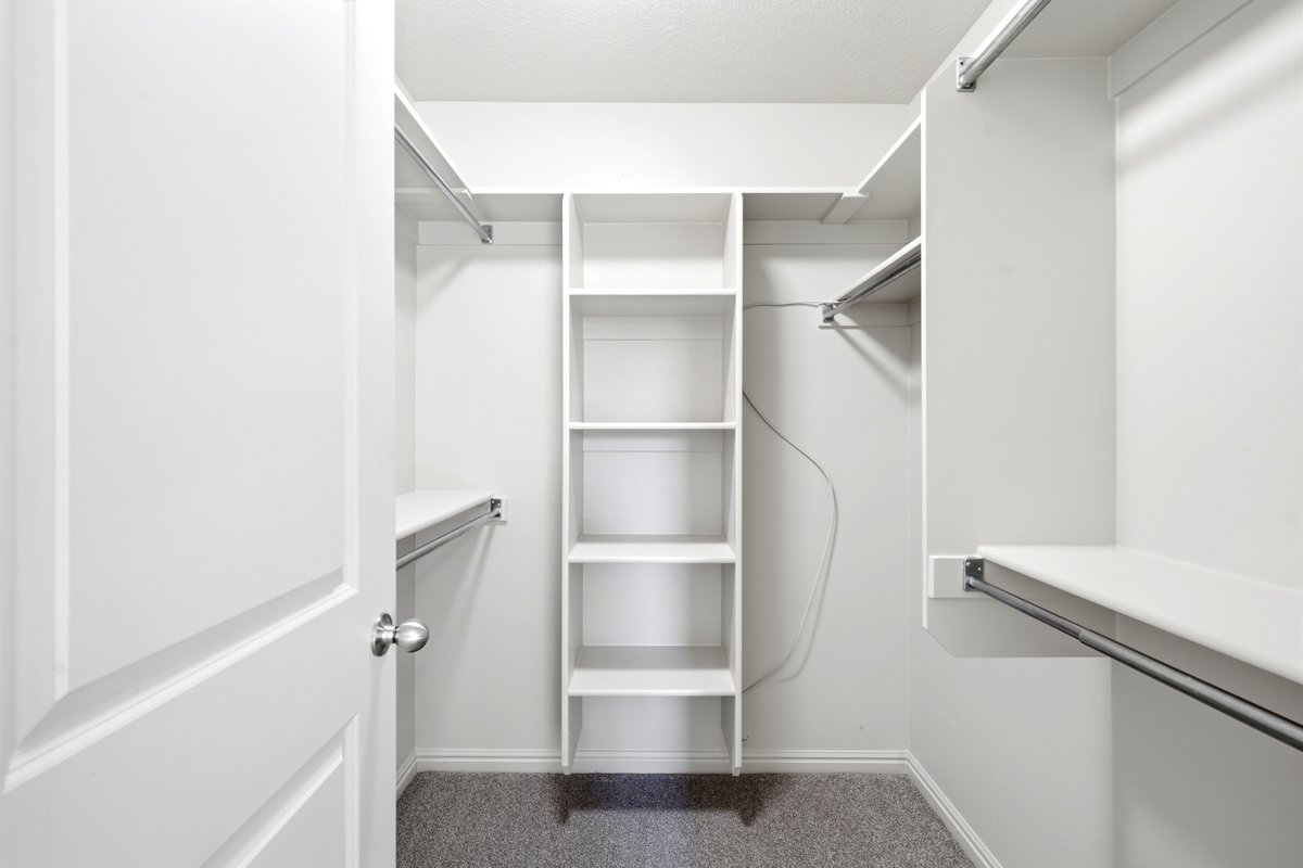 Walk-in closet featuring built-in shelving, multiple hanging rods, white trim, and light grey carpeting