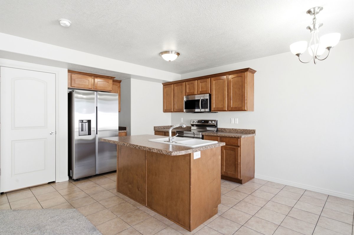 Kitchen featuring a central island with a built-in sink, wood-finish cabinetry, stainless steel appliances, and tile flooring