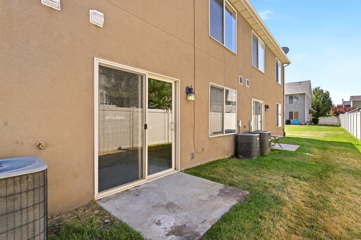 Rear exterior featuring a sliding glass door, a concrete patio, a stucco facade, a fenced yard, and multiple window openings