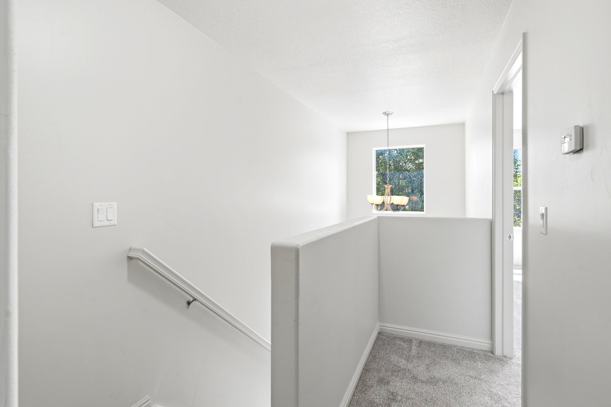 Upper-level landing featuring light gray carpeting, white painted walls, a simple white handrail, and a window with a suspended light fixture