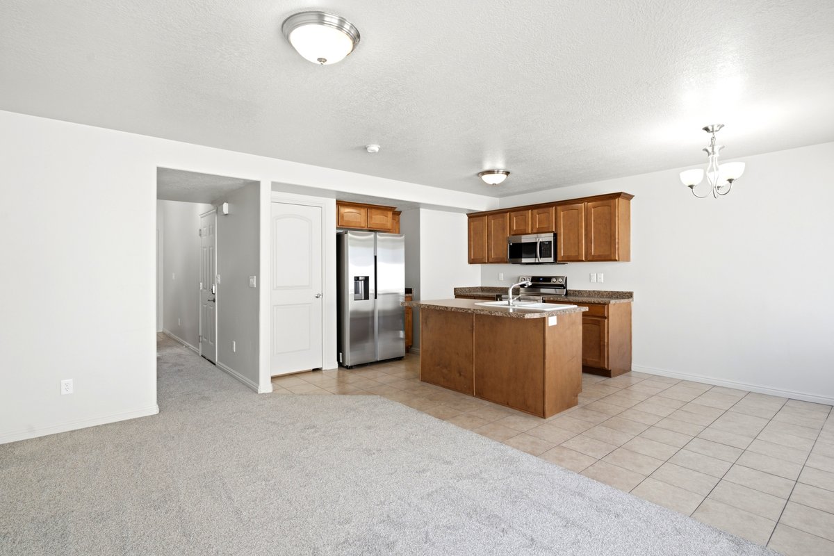 Open-concept kitchen featuring wood cabinetry, stainless steel appliances, a central island with an integrated sink, and stone-look countertops