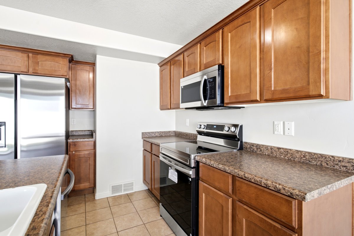 Kitchen featuring stainless steel appliances, wood cabinetry, stone-finish countertops, and tile flooring