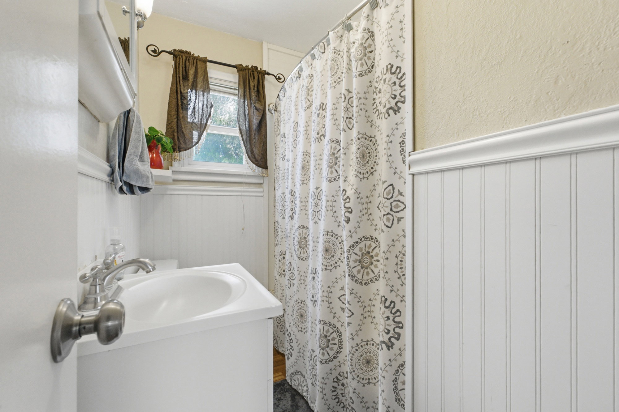 Bathroom featuring white beadboard paneling, a single vanity with an integrated sink, and an overhead light fixture, window for natural light, and shower/tub combination.