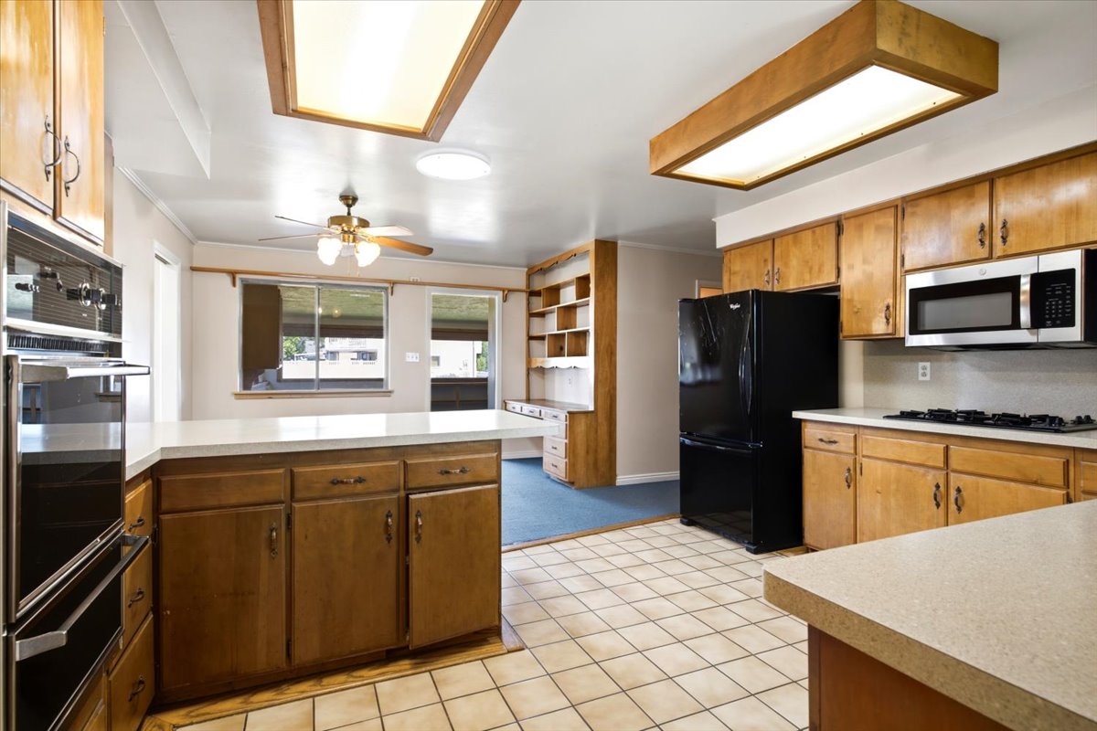 Kitchen featuring wood cabinetry, light-toned countertops, tile flooring, and stainless steel appliances