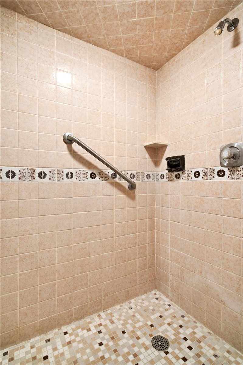 Tiled shower with a decorative mosaic accent band, integrated corner shelf, and a grab bar