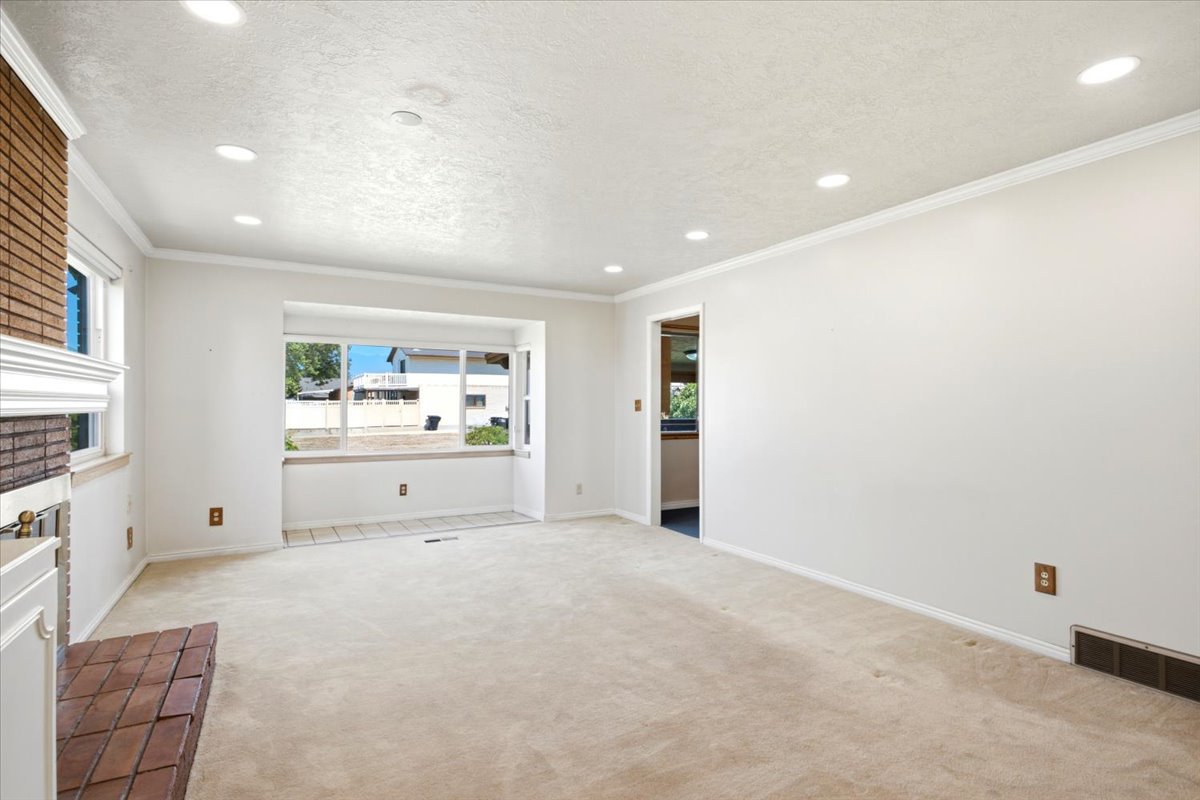 Spacious living area featuring a bay window with tiled flooring, neutral-toned carpet, recessed lighting, and a brick fireplace