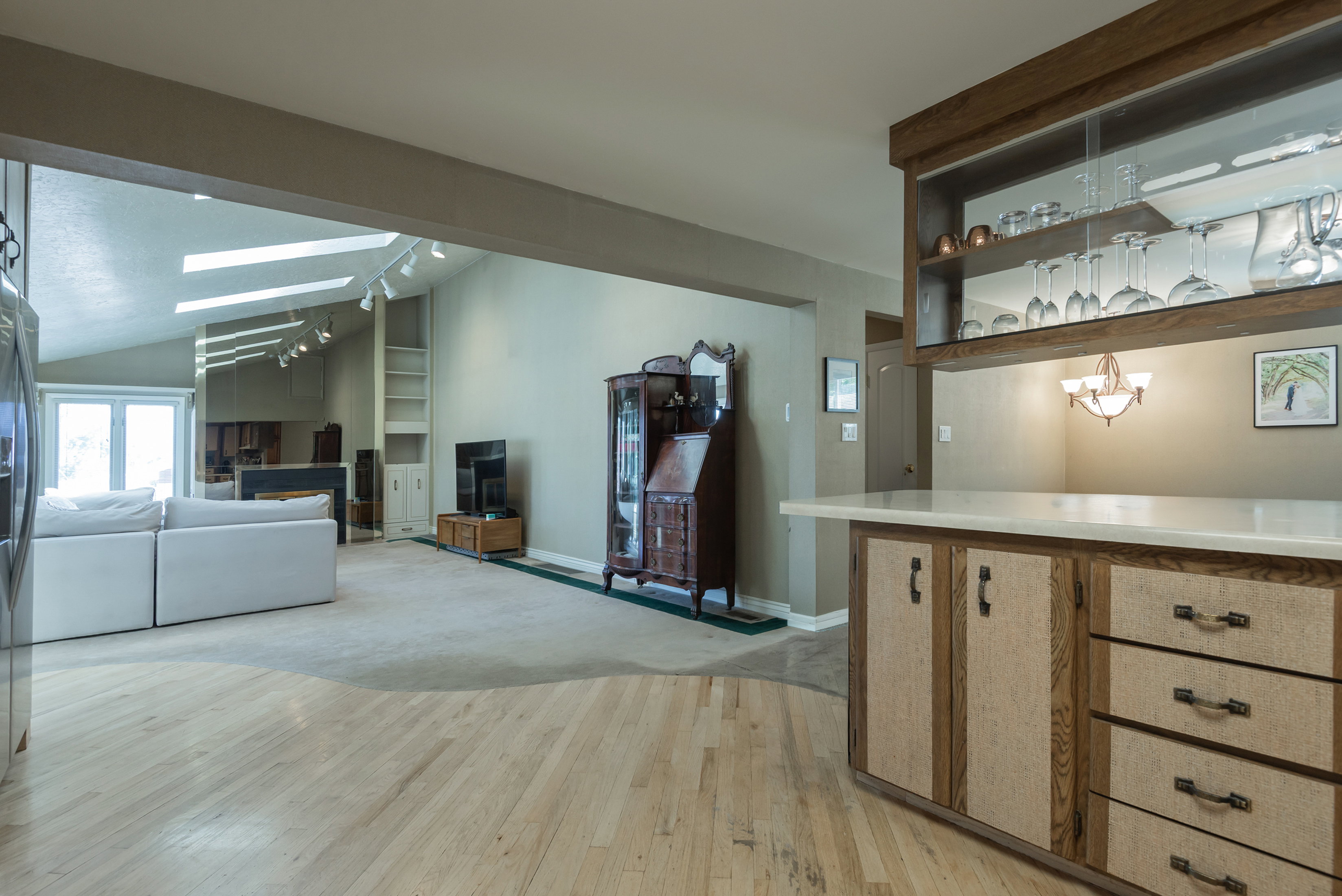 Built-in bar with a light-toned countertop, wood-finish cabinetry, and an upper display cabinet with glass shelving