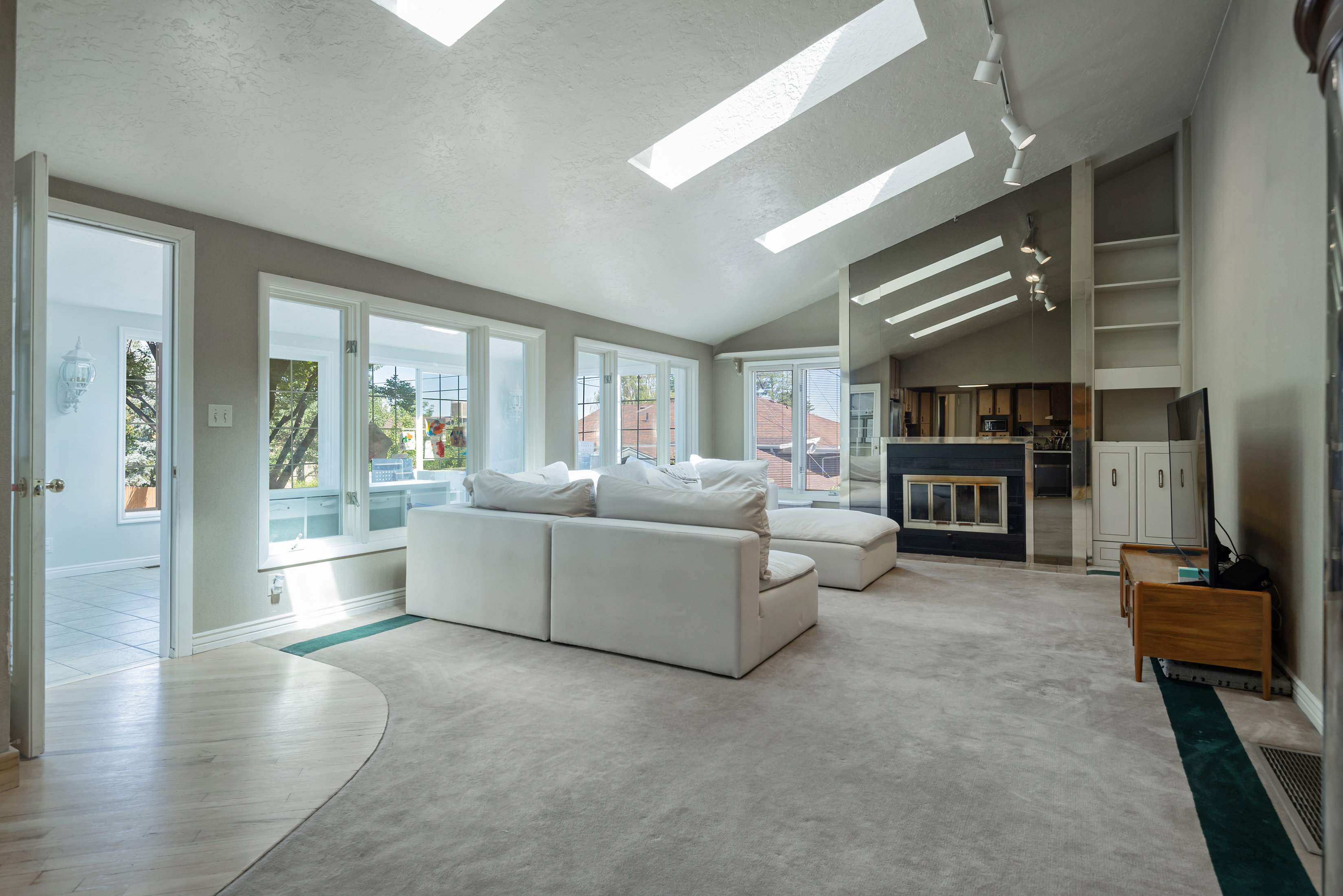 Spacious living area featuring a vaulted ceiling with multiple skylights, extensive window line, and light-colored carpeting