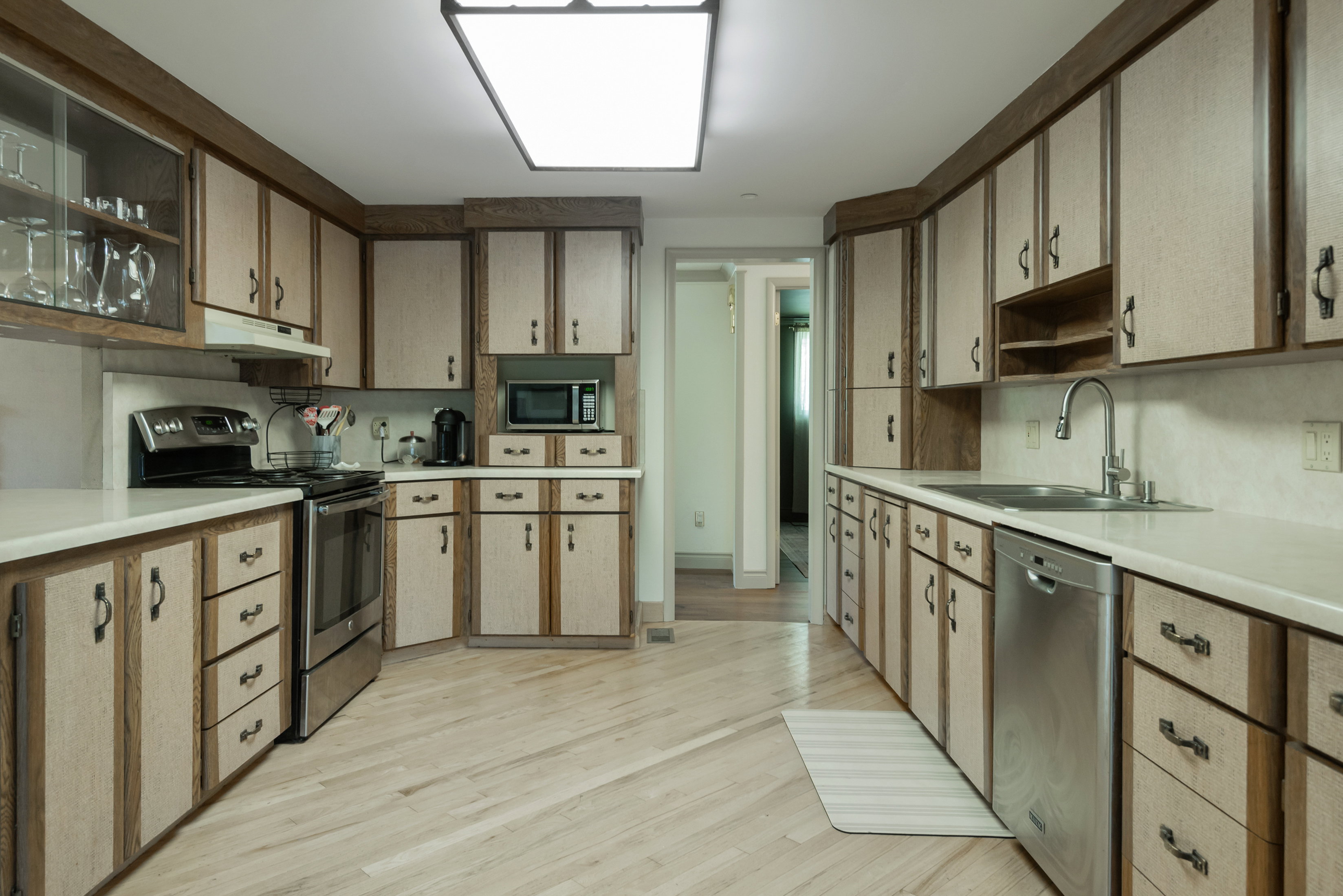 Kitchen featuring extensive cabinetry with wood-finish trim, light-toned wood-finish flooring, white countertops, stainless steel appliances, and a rectangular ceiling light fixture