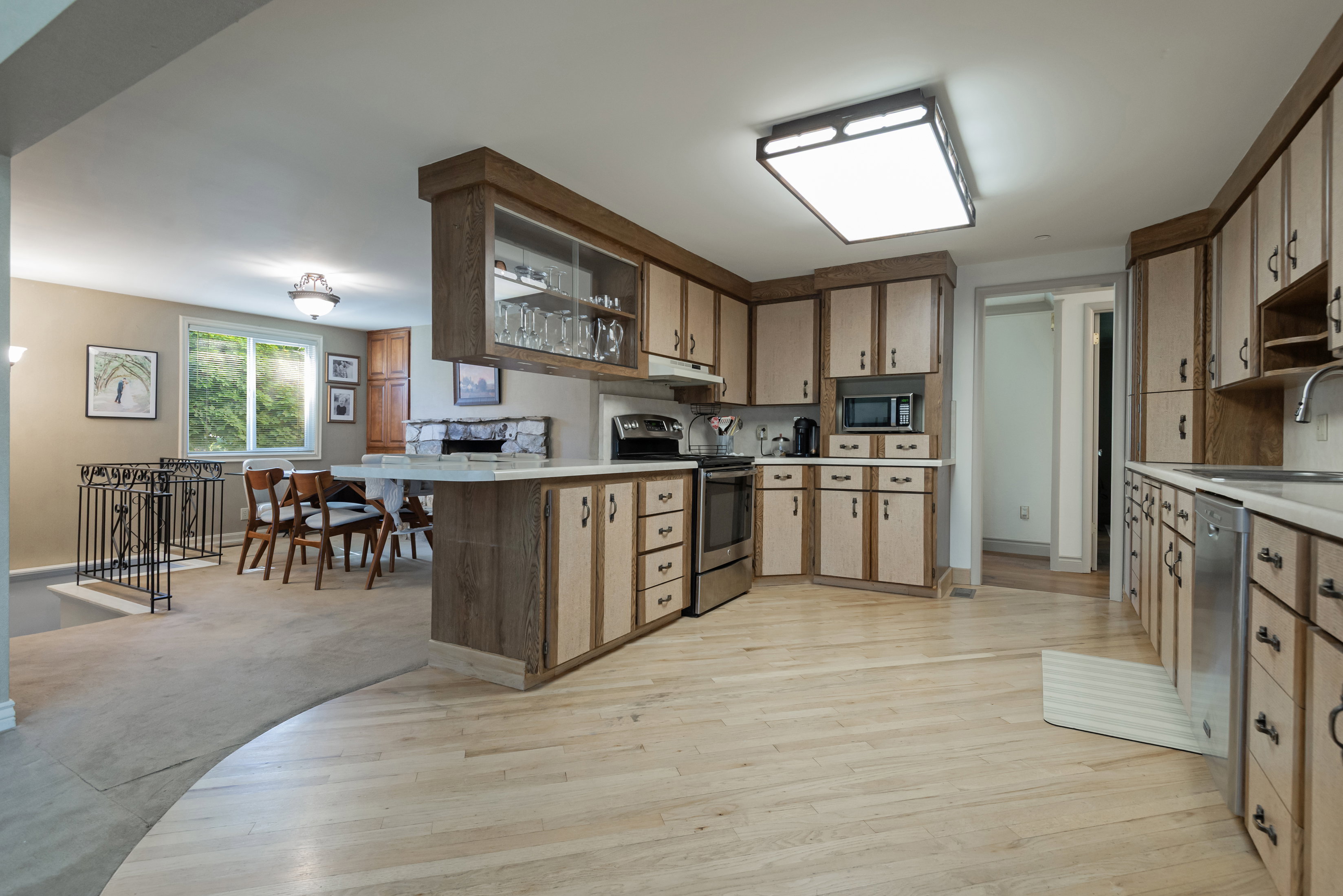 Spacious kitchen featuring light wood-finish flooring, extensive cabinetry with integrated display shelves, stainless steel appliances, and a peninsula counter with seating
