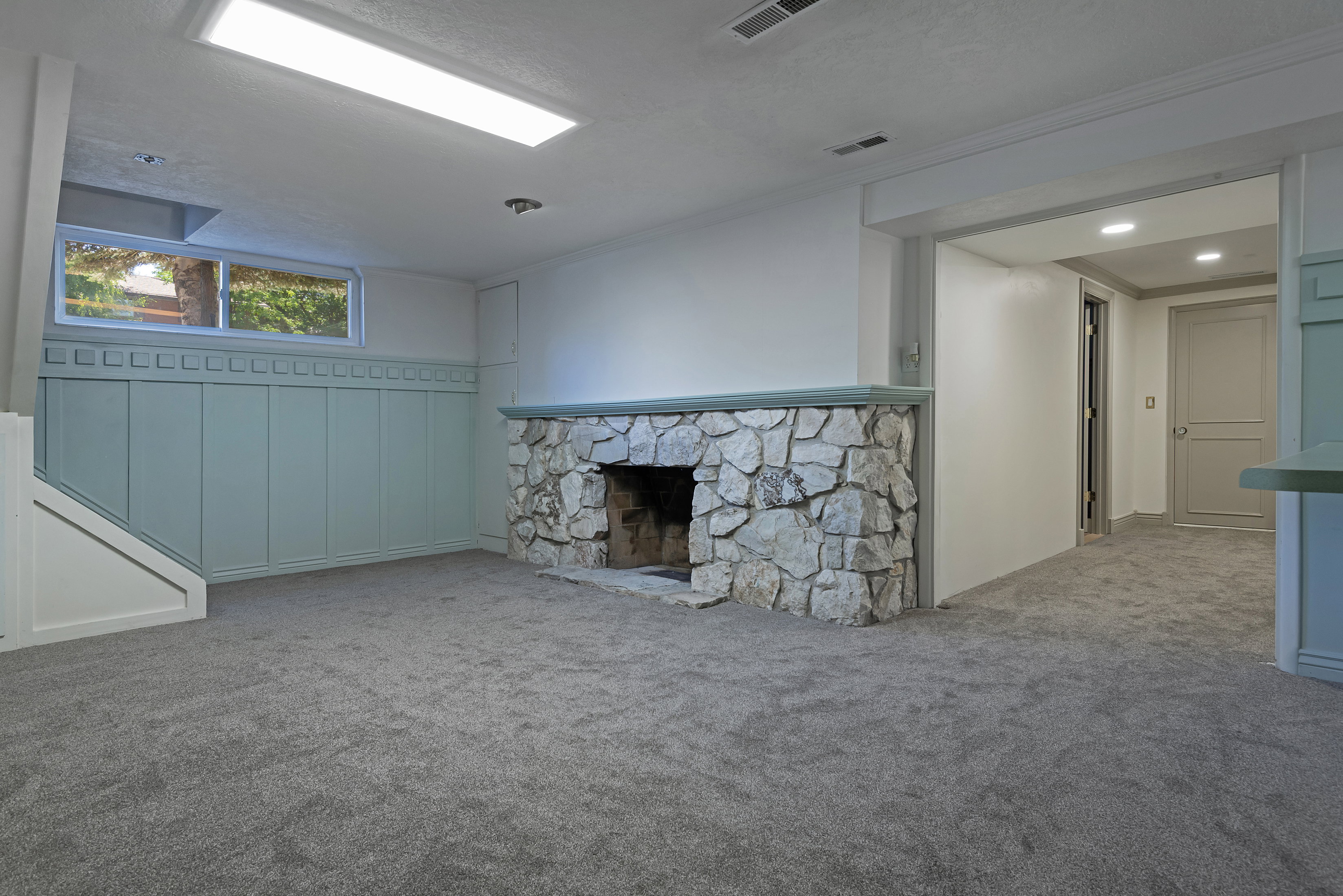 Spacious room featuring a stone-clad fireplace with a light green mantel, coordinating wainscoting, light gray carpet, a built-in window, and recessed lighting