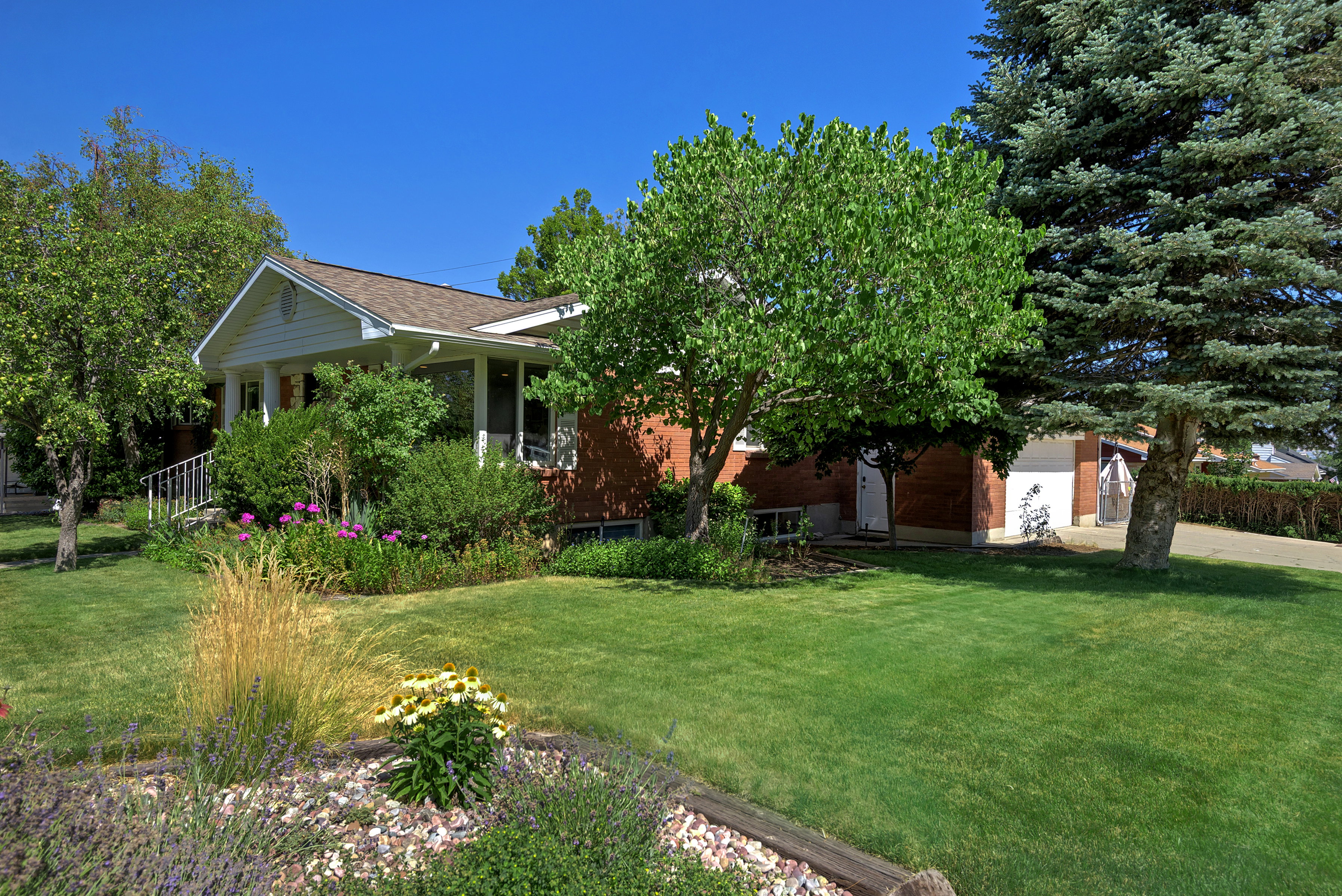 Brick home featuring a white-gabled entry porch, mature landscaping, and an attached garage