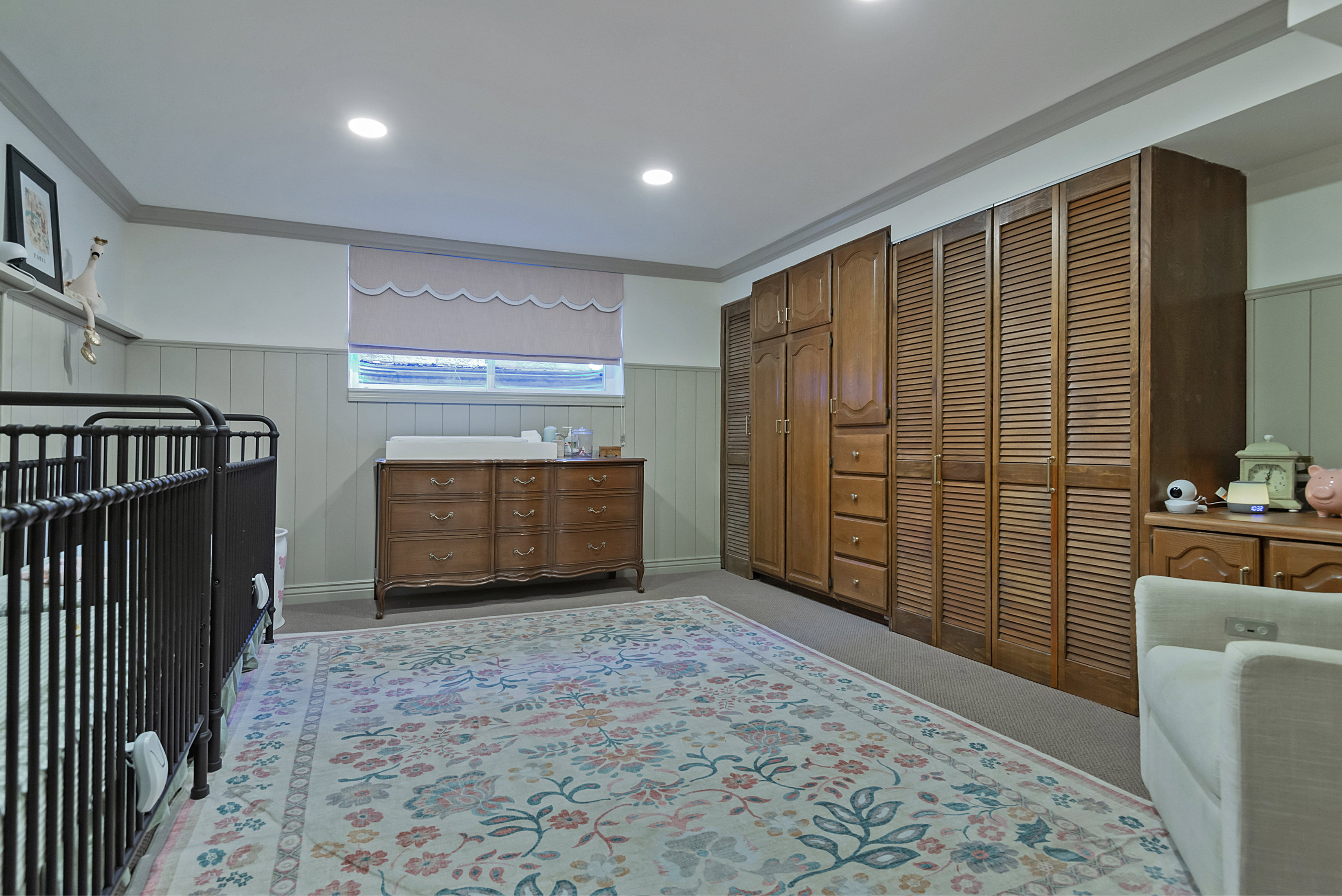 Recessed lighting illuminates a room featuring wainscoting, a window with a valance, and extensive built-in wood cabinetry