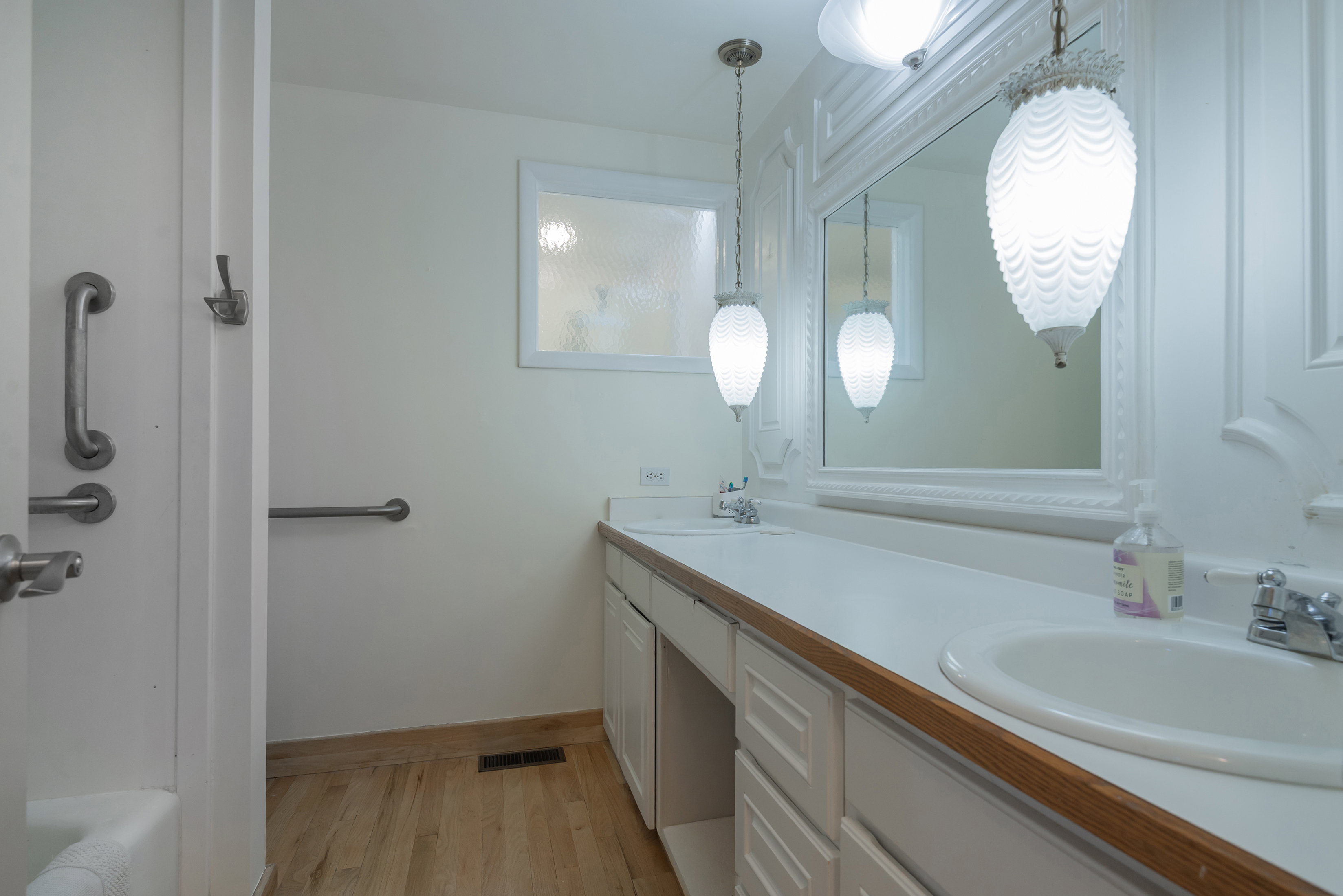 Double vanity featuring white cabinetry, integrated sinks, a generous countertop, and wood-finish flooring