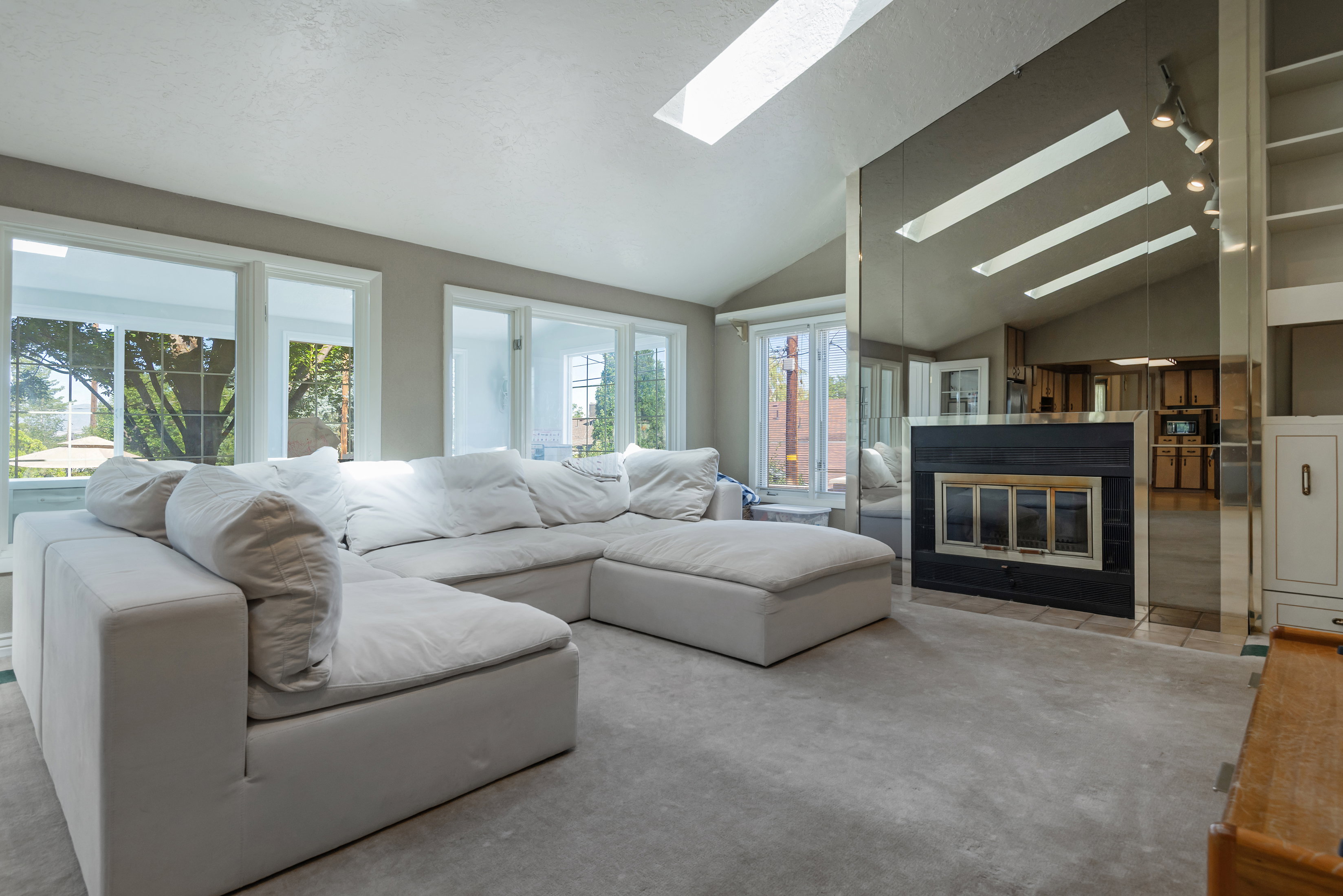 Living area featuring a vaulted ceiling with skylights, multiple large windows, a built-in fireplace with a dark surround, and an integrated mirrored wall
