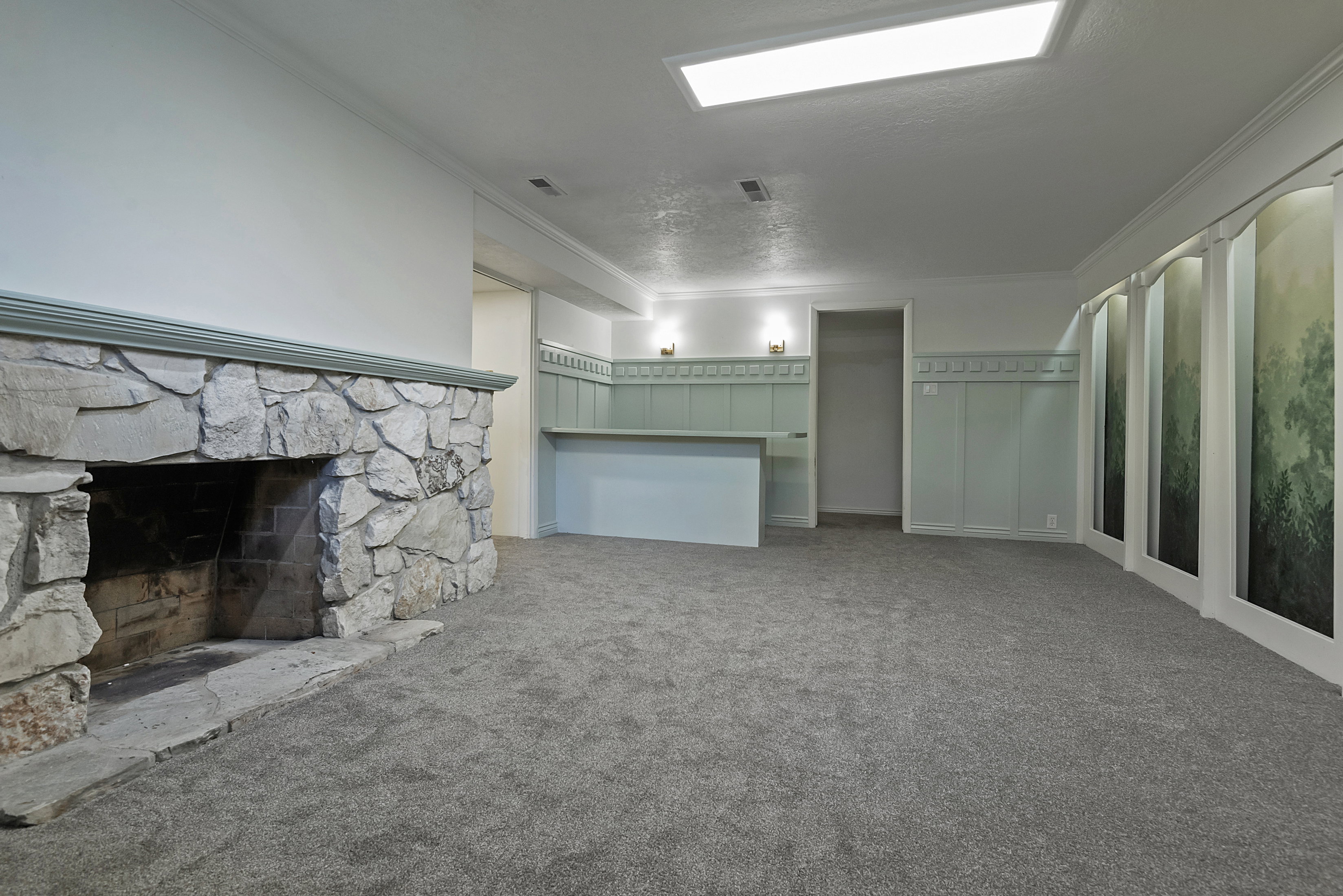 Spacious room featuring a large stone fireplace, gray carpeting, recessed lighting, and a built-in bar with sconce lighting