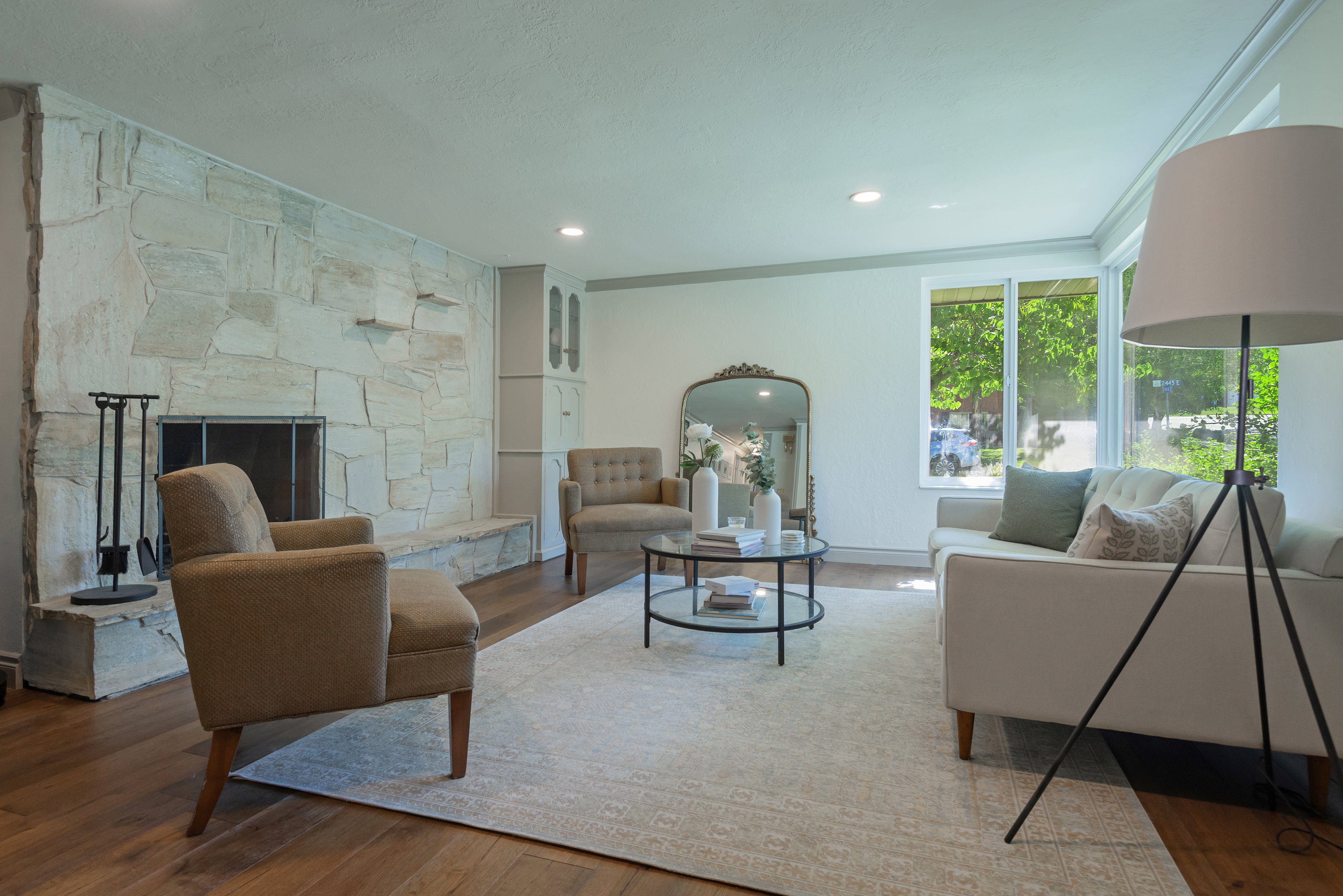 Living area featuring a floor-to-ceiling stone fireplace, recessed lighting, wood-finish flooring, white trim, and large windows