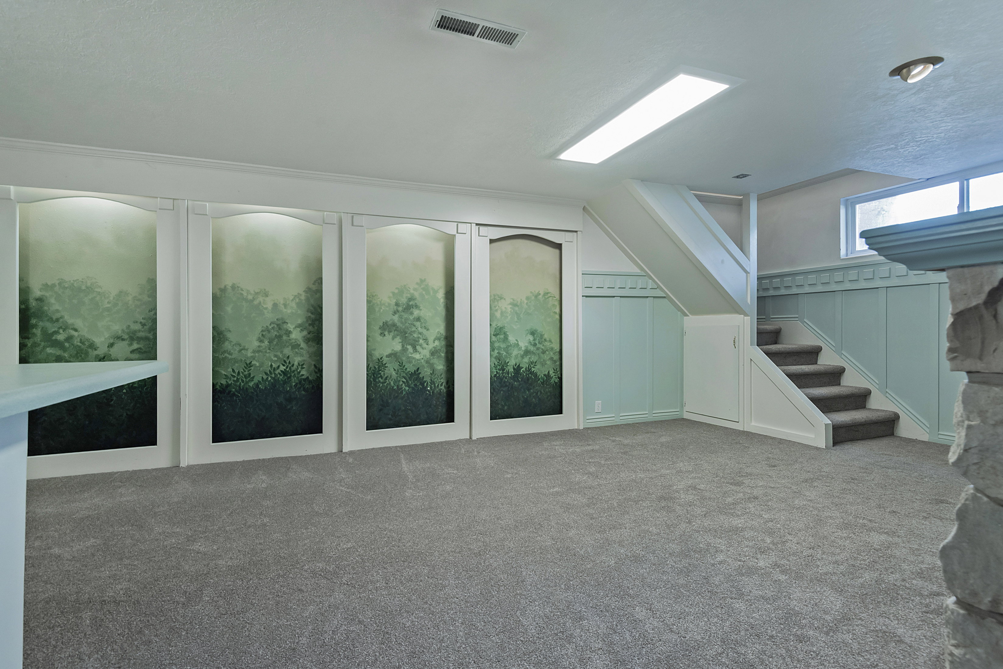 Spacious room featuring gray carpet flooring, recessed lighting, and a prominent staircase with white trim