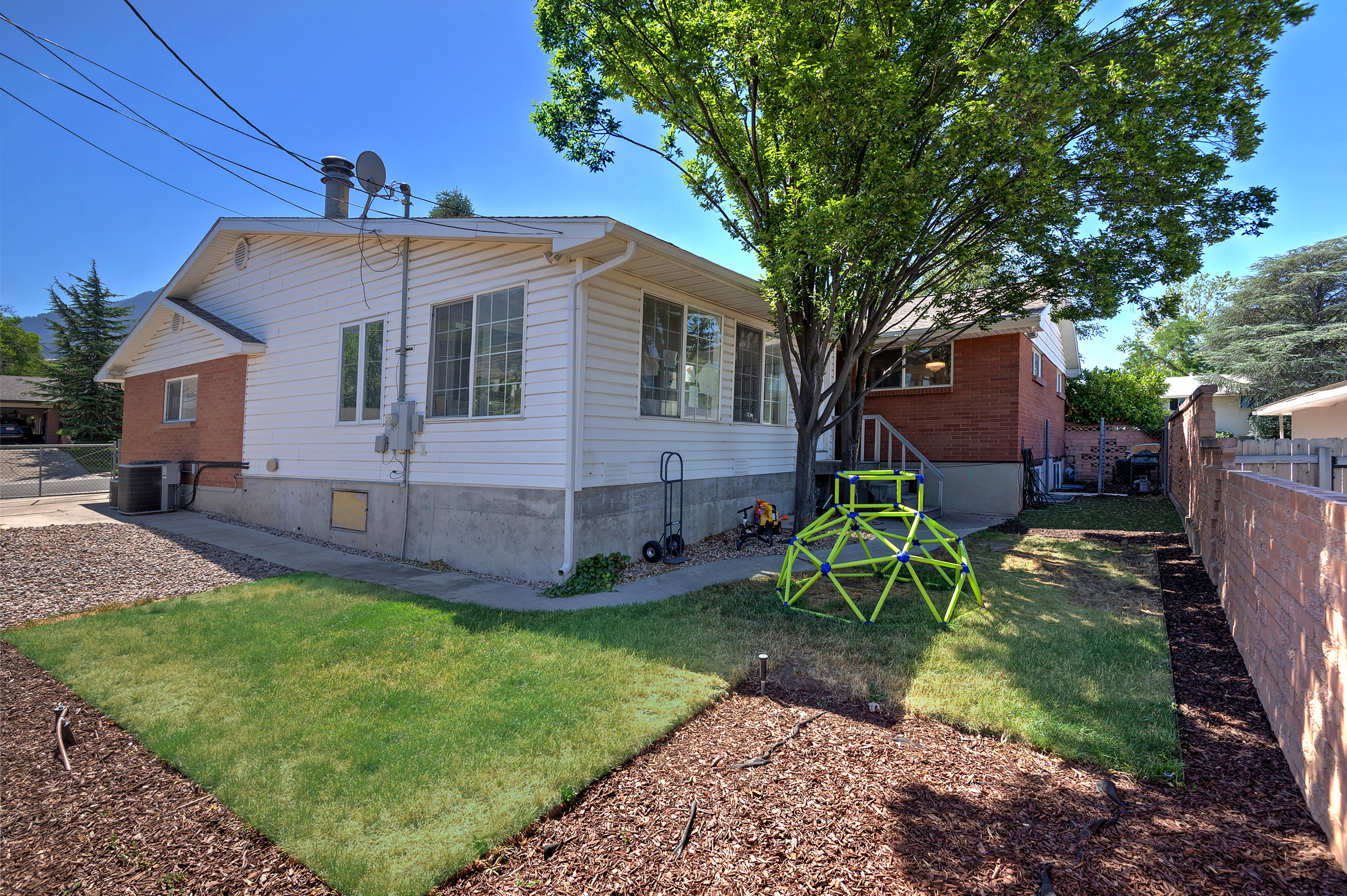 Spacious backyard featuring a manicured lawn, established mature tree, brick and siding exterior, and a concrete pathway