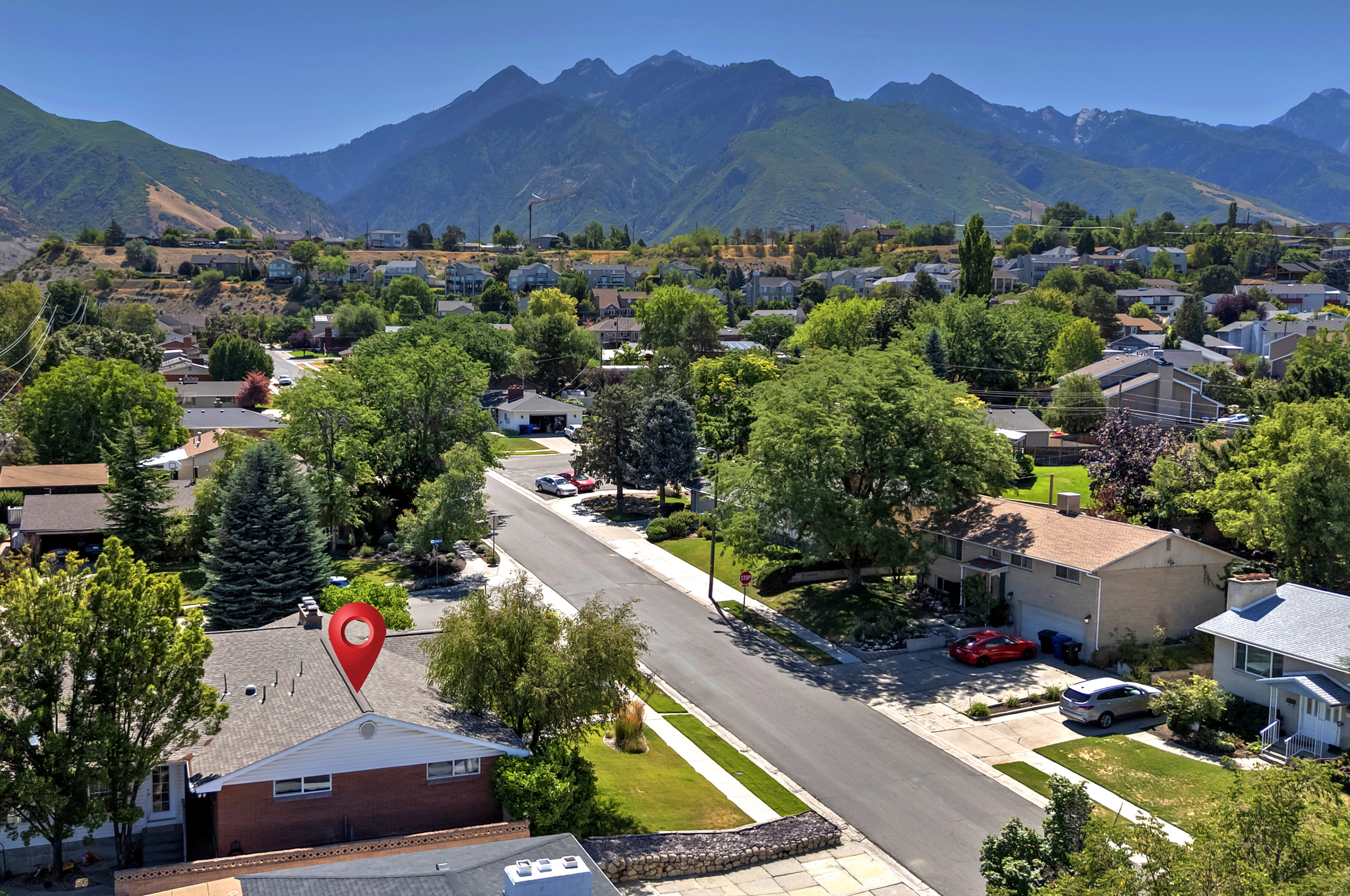 Residential street with established landscaping, mature trees, and mountain scenery